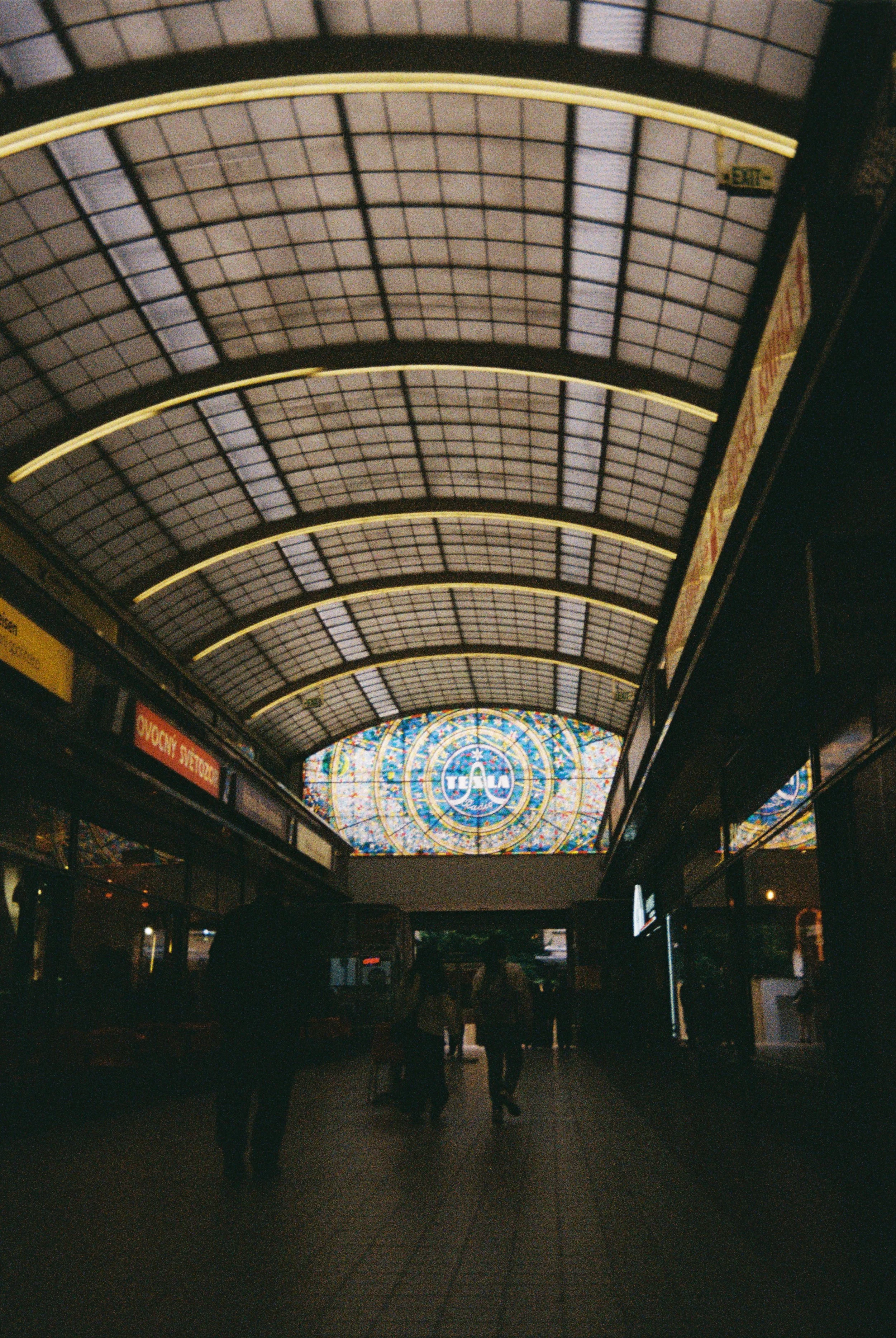 People walking inside an airport terminal with a large stained glass window and a decorative ceiling.