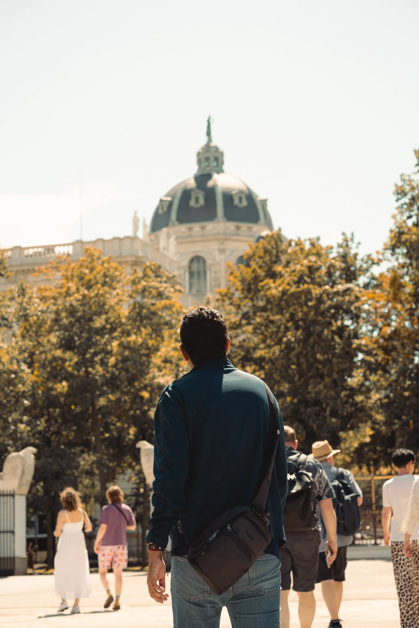 Man with backpack standing in a crowded outdoor area with the U.S. Capitol building in the background during daytime.