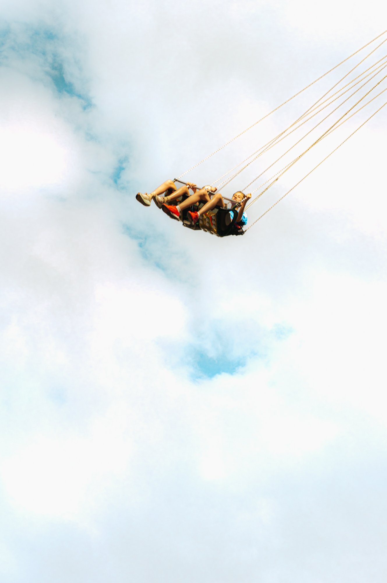 Child on a swing ride at an amusement park against a partly cloudy sky.