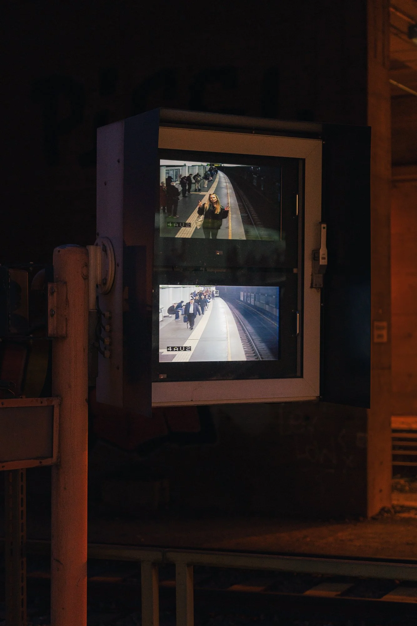 Reflection of a woman taking a selfie at a subway station platform, viewed through a screen with two train station images, at night.