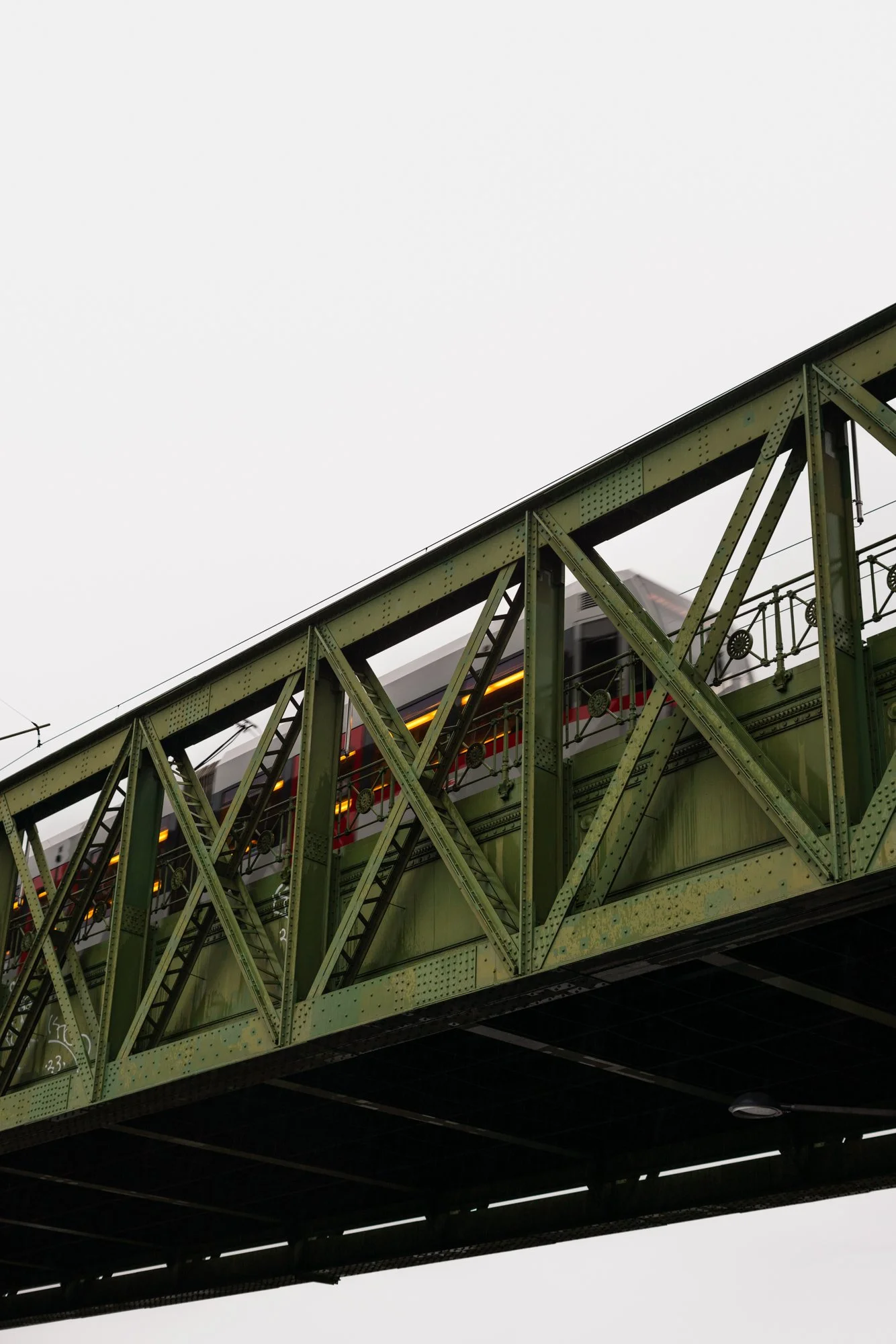 A train passing over a green steel bridge structure against a cloudy sky.