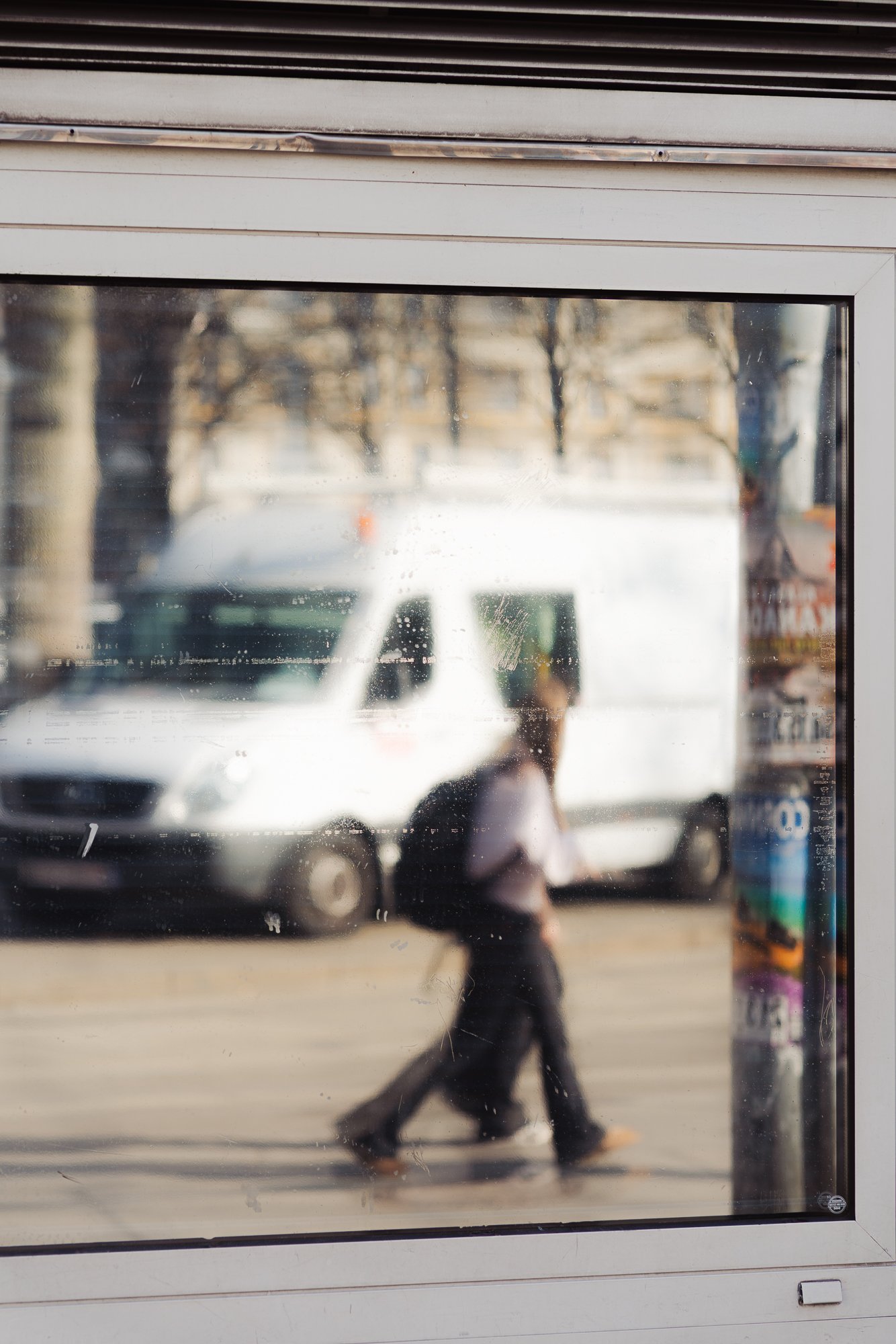 View through a glass window showing a blurred street scene with a person walking, cars, and trees outside.
