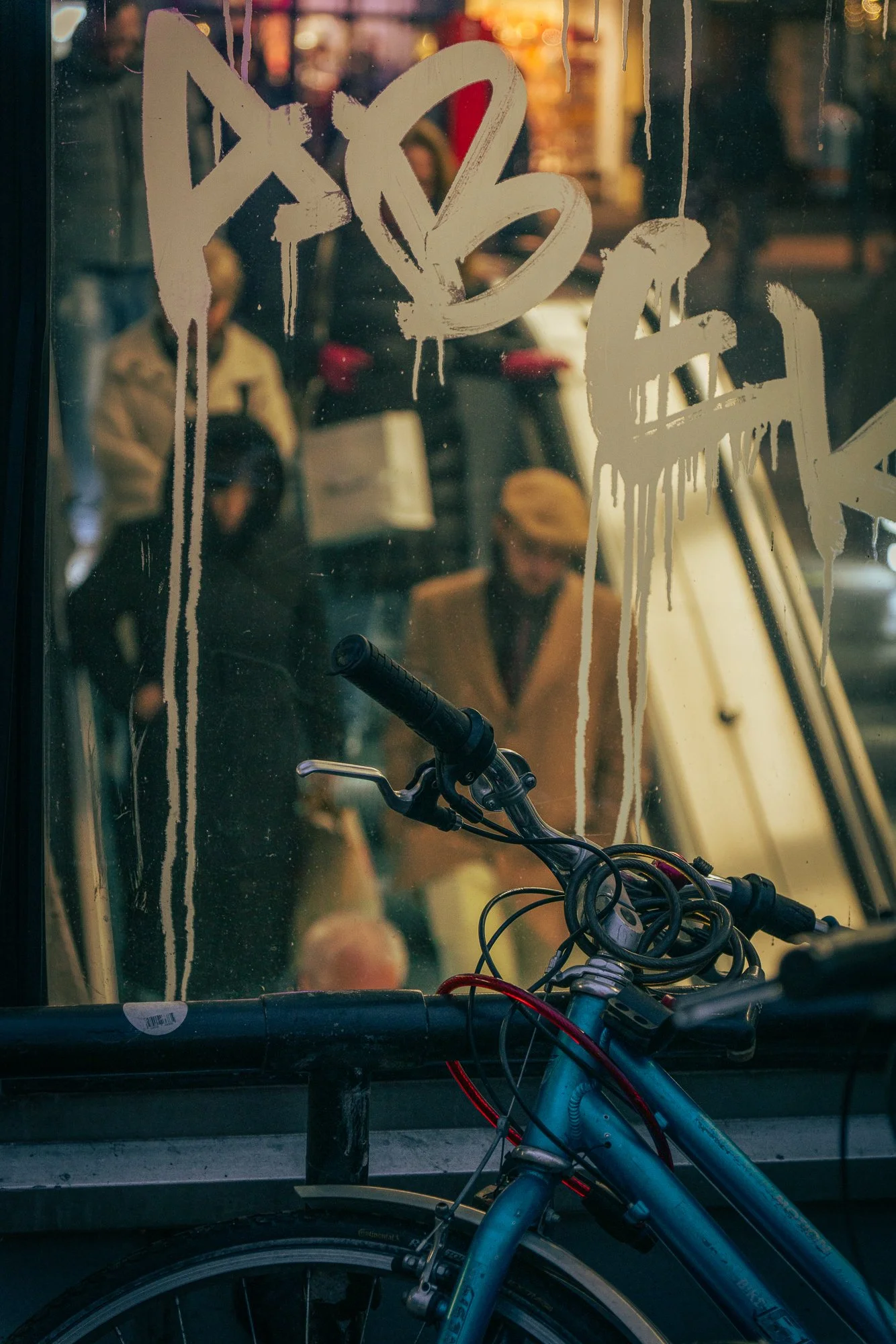 A bicycle with its handlebars and part of the frame in front of a glass window or door with handwritten graffiti that seems to say 'D A R K'. The bike's seat and rear wheel are visible at the bottom of the image.