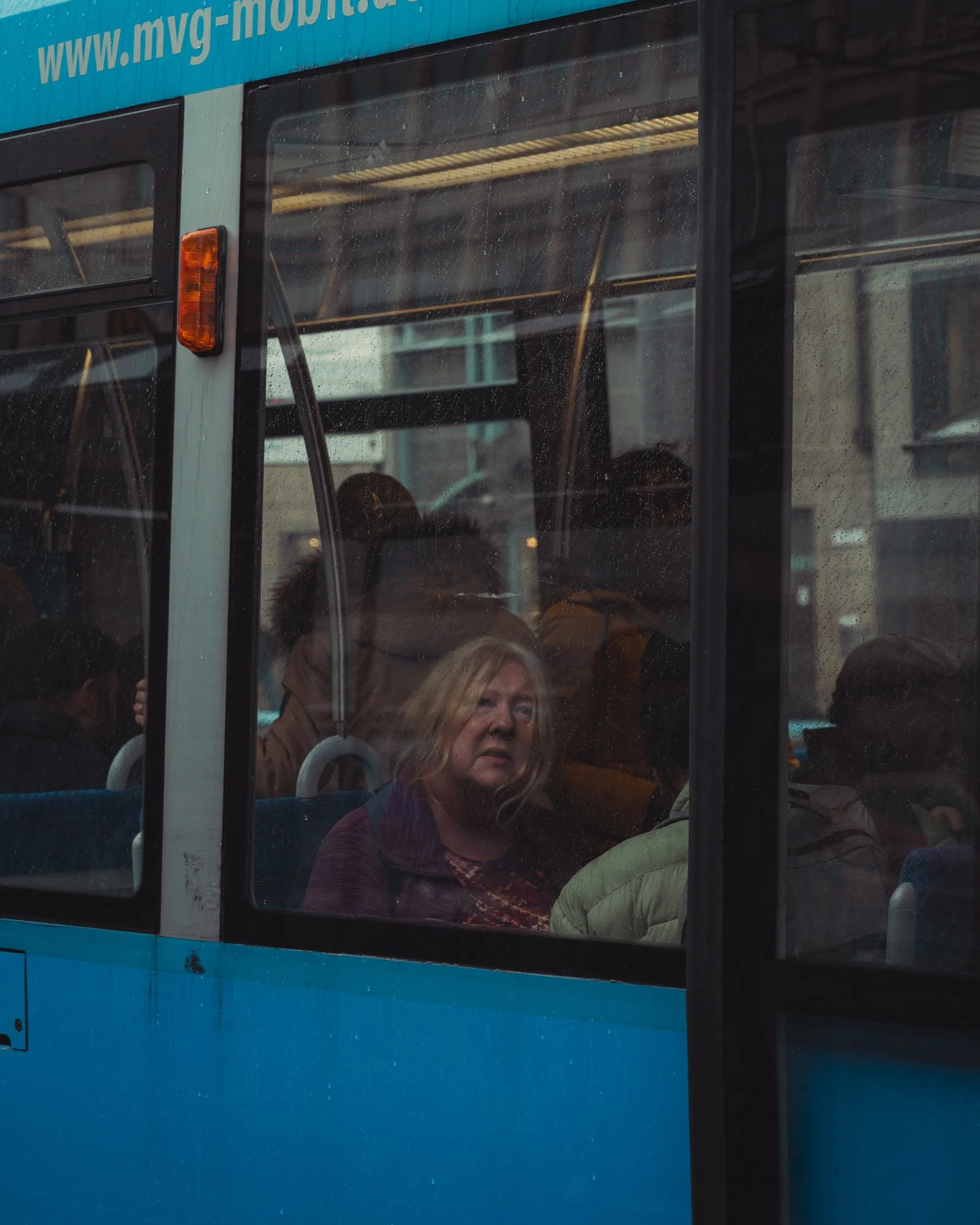 A woman with blonde hair looking out the window of a blue and black city bus.