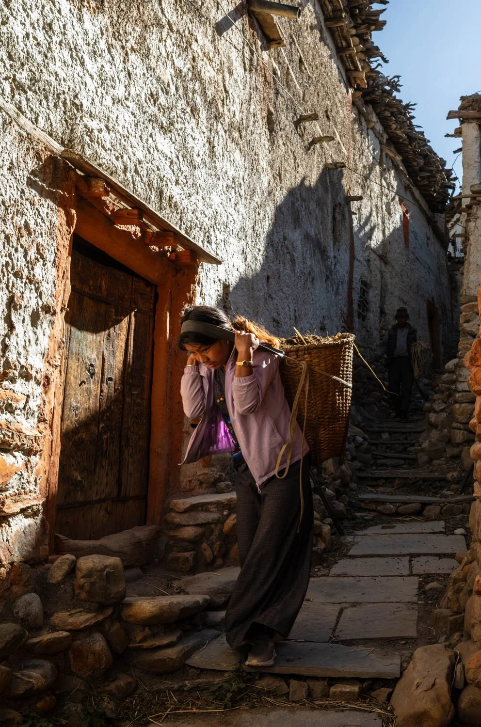 A girl carries a basket secured by a strap around her forehead in the Mustang village of Tangbe