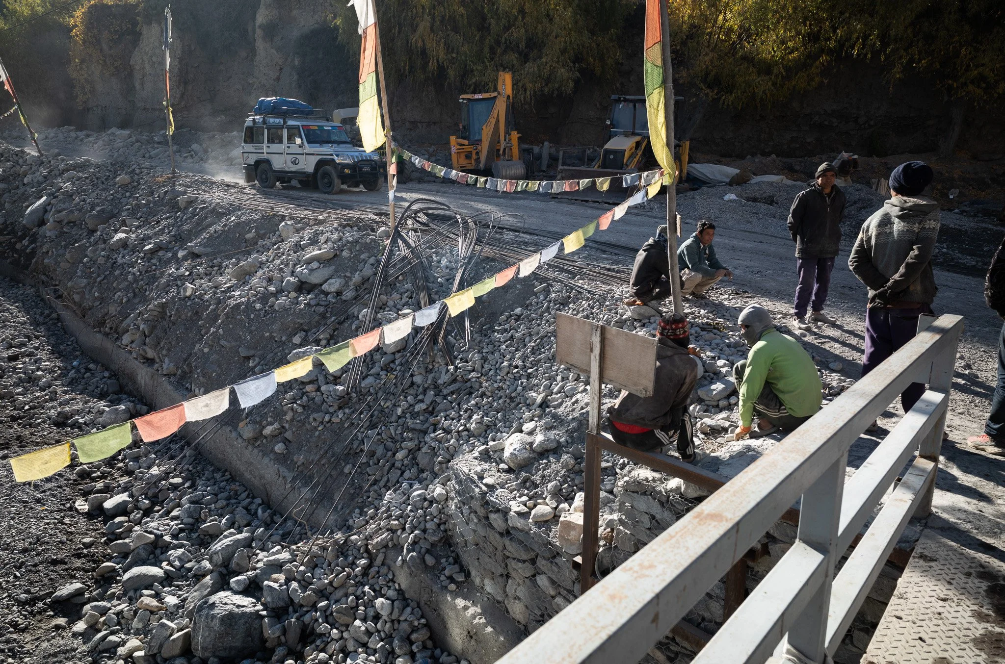 Group of workers at a construction site working on a rocky embankment, with construction vehicles and equipment in the background.