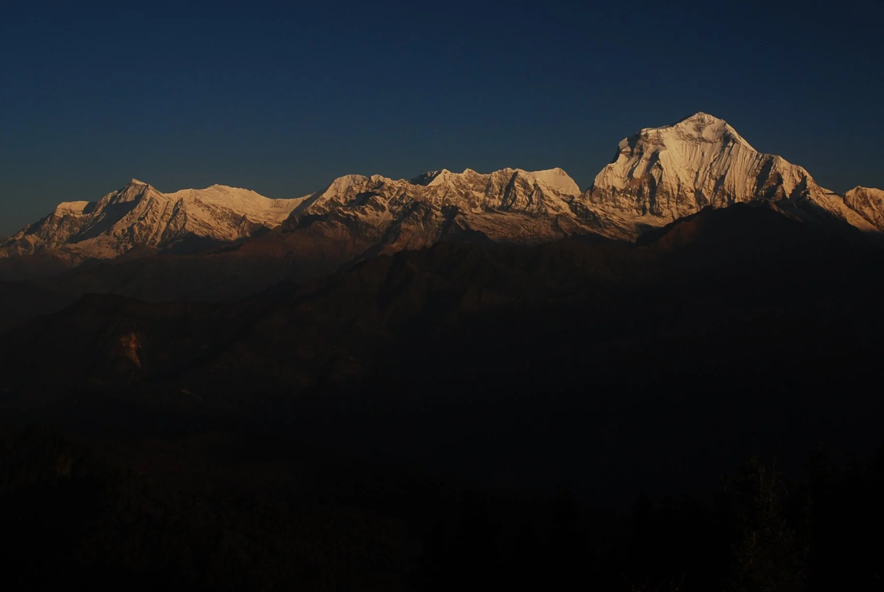 Snow-capped mountain range at sunrise or sunset, with dark foreground hills.