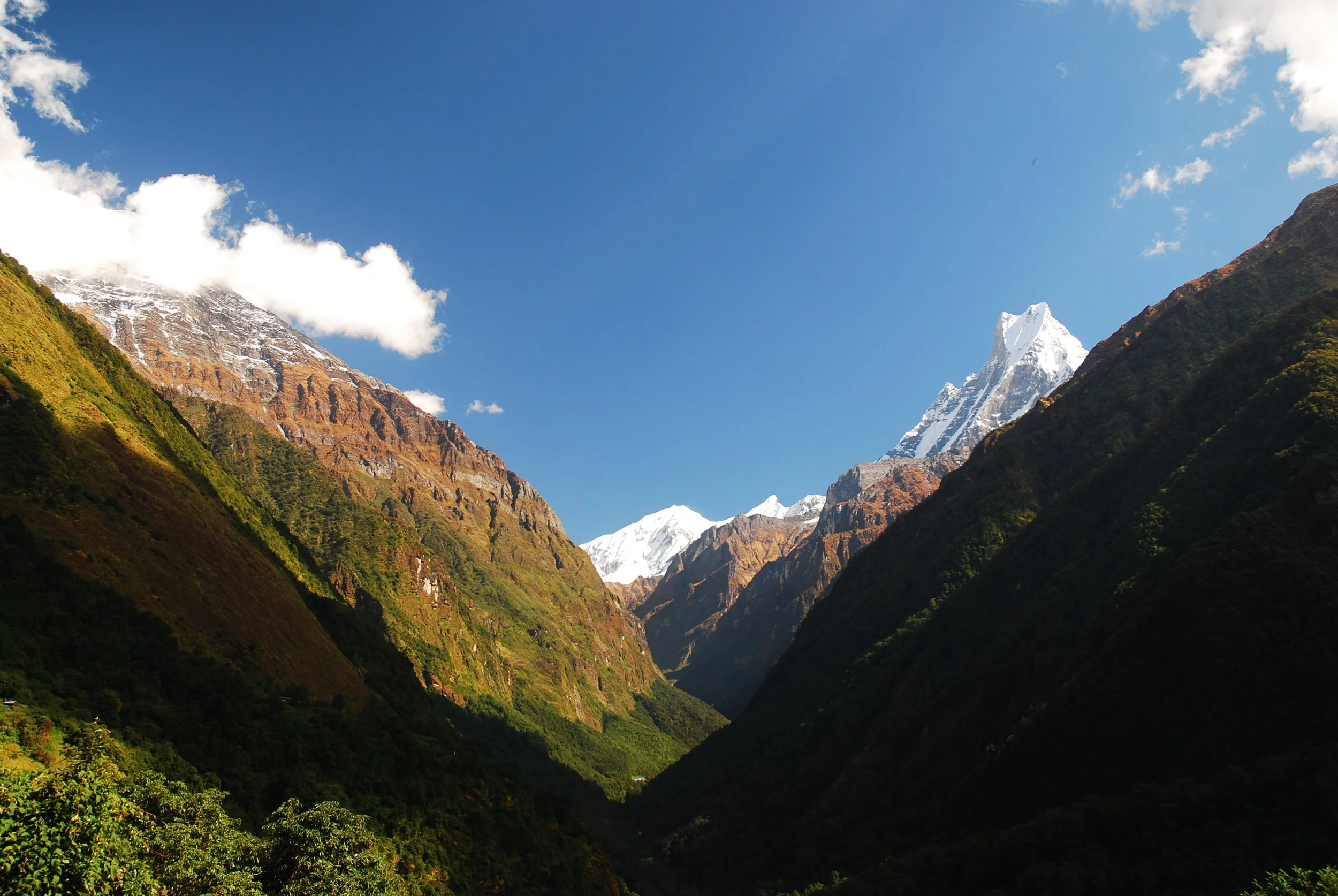 Scenic view of snow-capped mountains and green valleys under a clear blue sky.