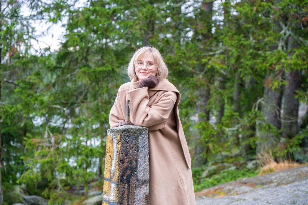 Venla Viitanen metsäisessä luonnossa nojaa kallioon ja hymyilee kameralle
