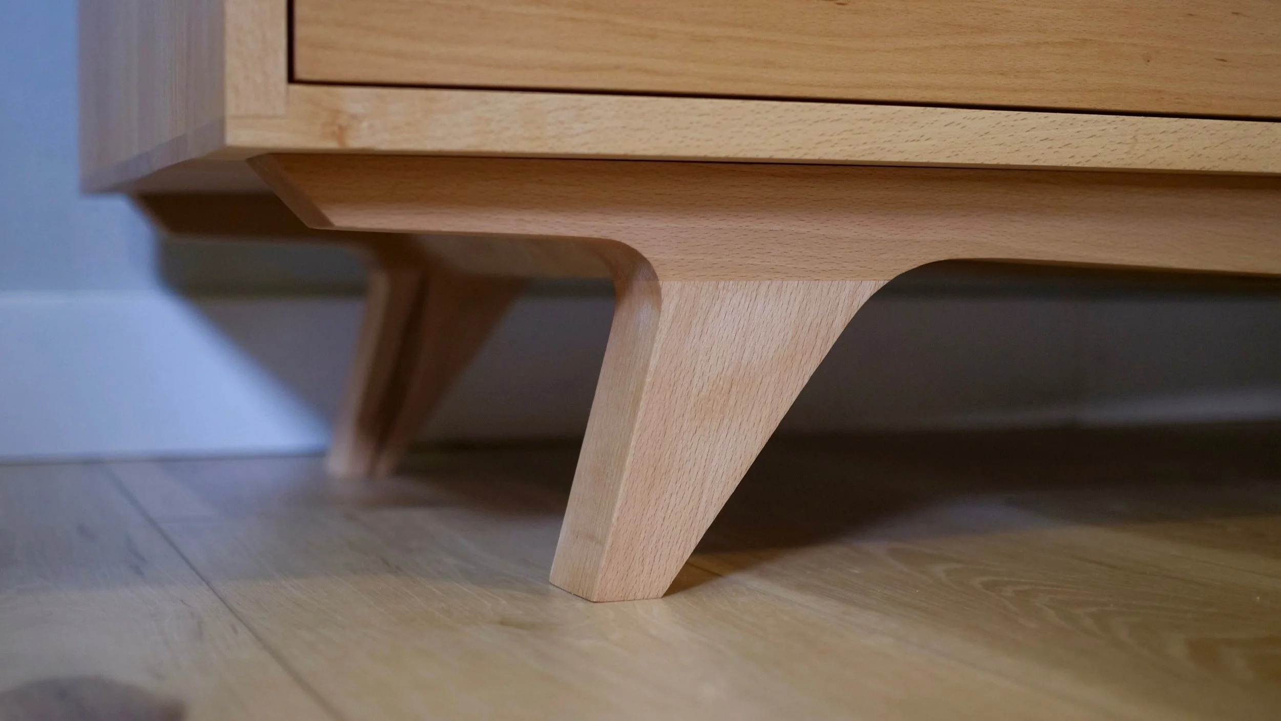 Close-up of the wooden leg of a piece of furniture, possibly a bed or a table, showing smooth, light-colored wood and a modern design.