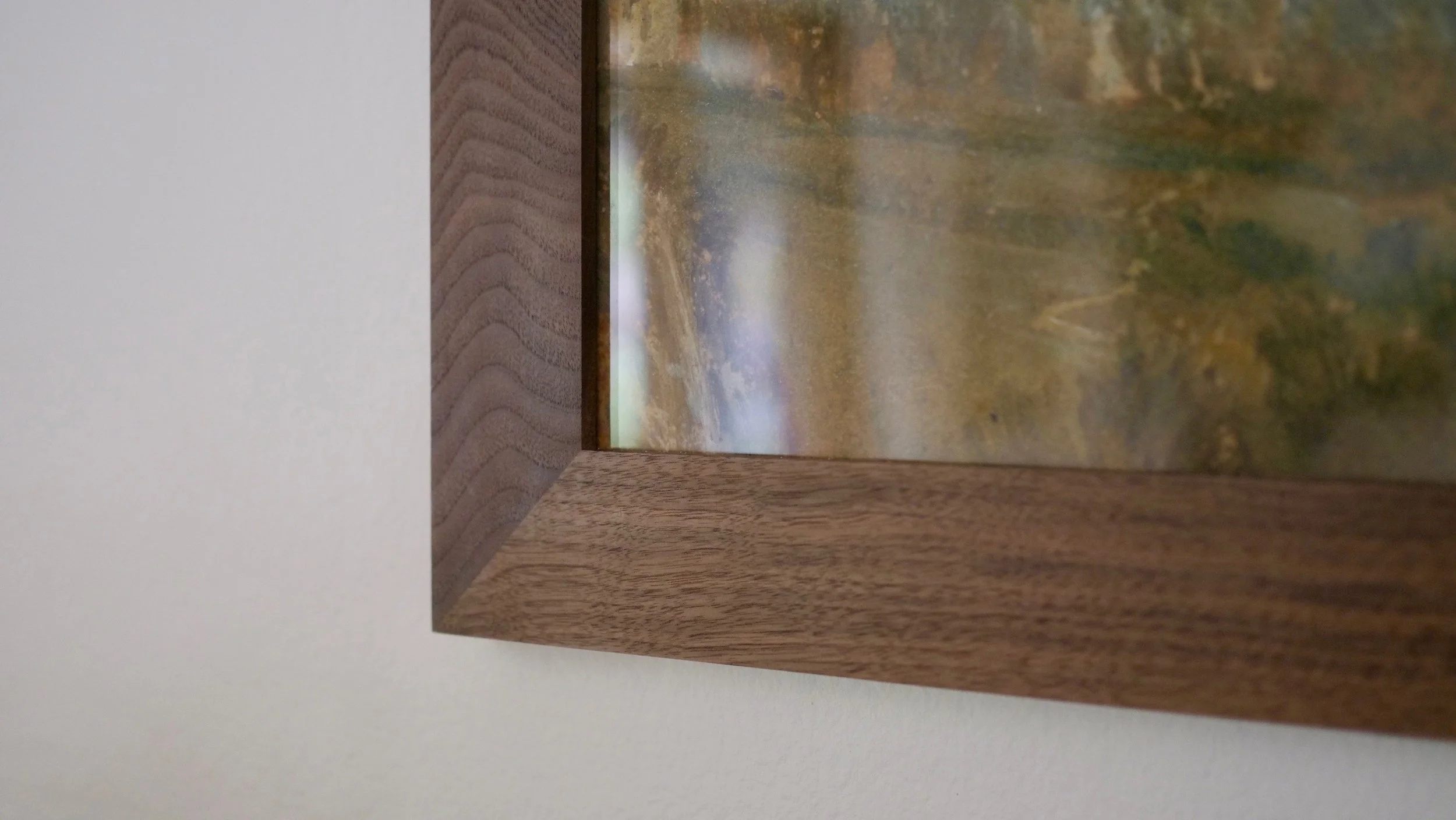 Close-up of a corner of a wooden frame with a landscape painting in the background.