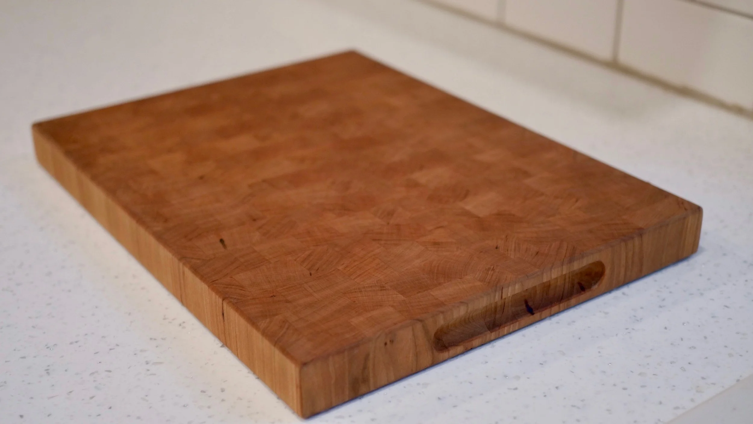 A wooden cutting board on a white kitchen countertop near a tiled backsplash.