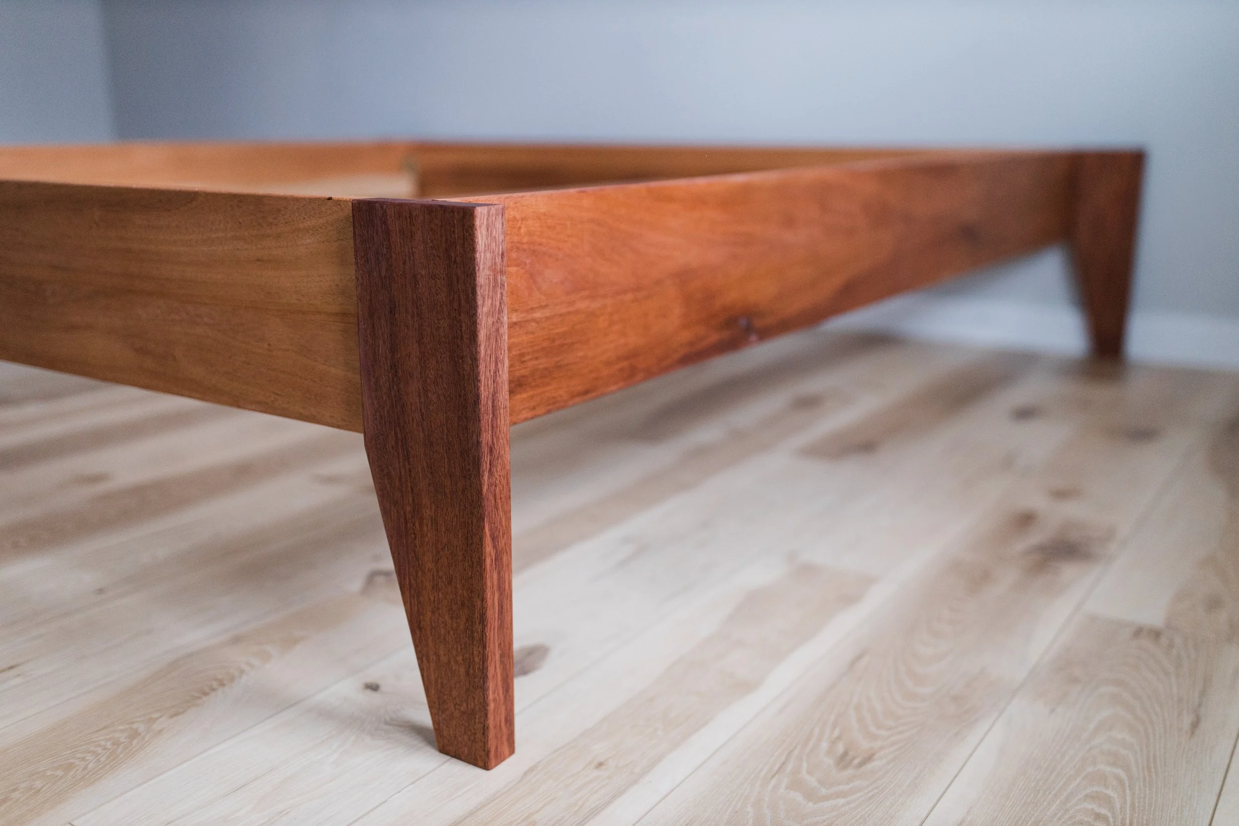 Close-up of a wooden bed frame with a simple, modern design on a light-colored wooden floor.