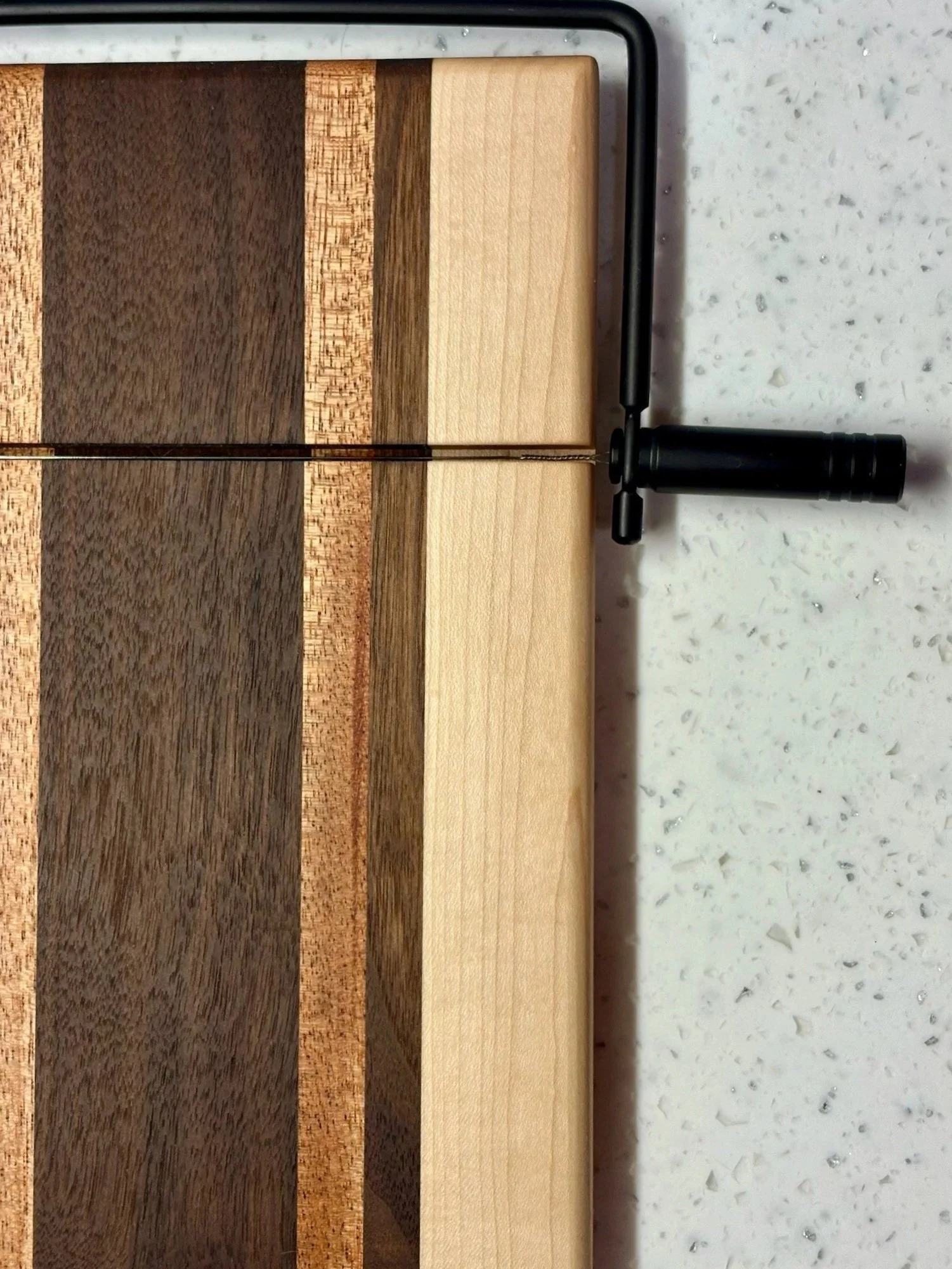 A chessboard with alternating dark and light wood squares and a black hand-held chess piece, a pawn, placed on the right side of the board.