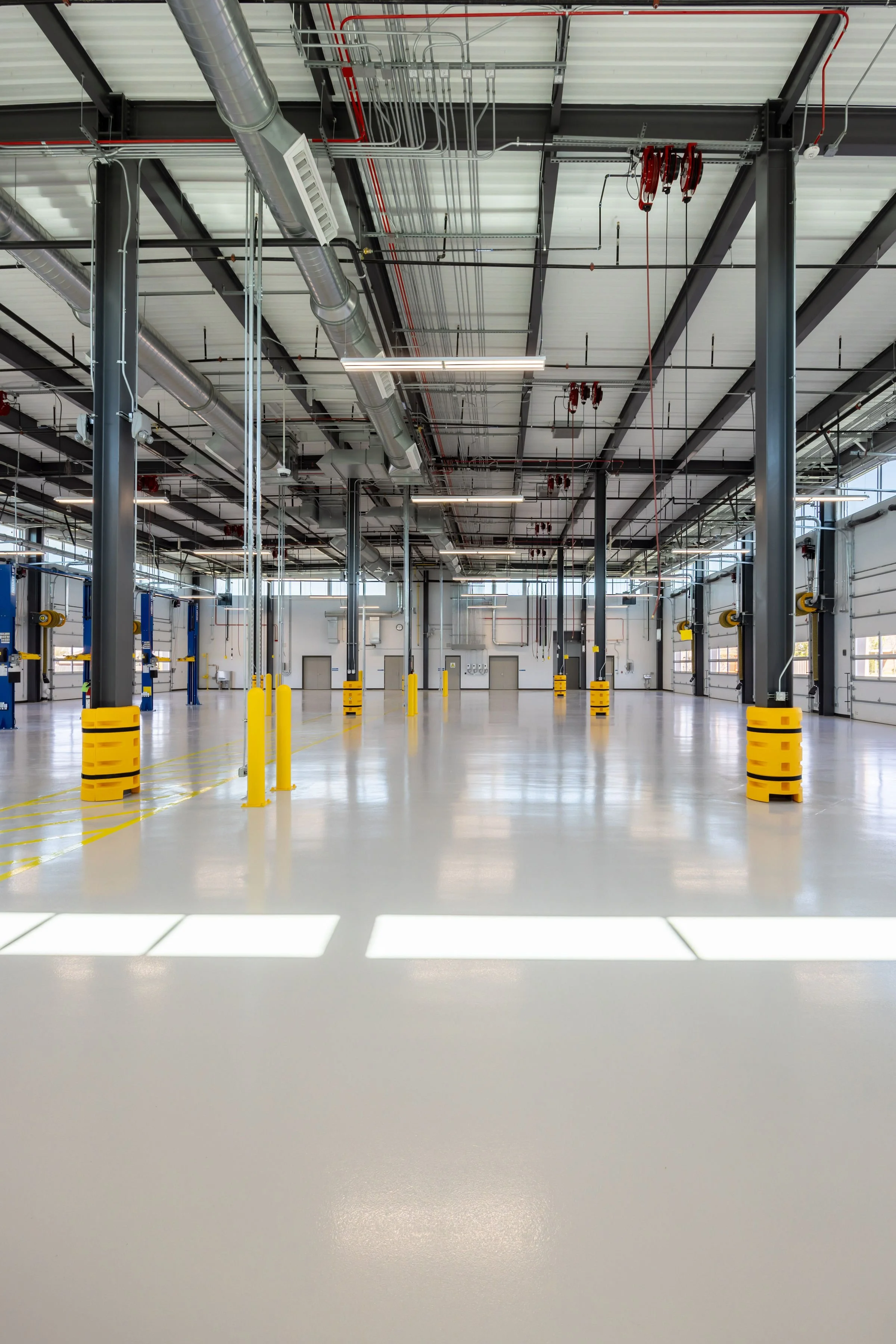 Empty industrial warehouse with high ceilings, metal support beams, and large garage doors, well-lit with natural light