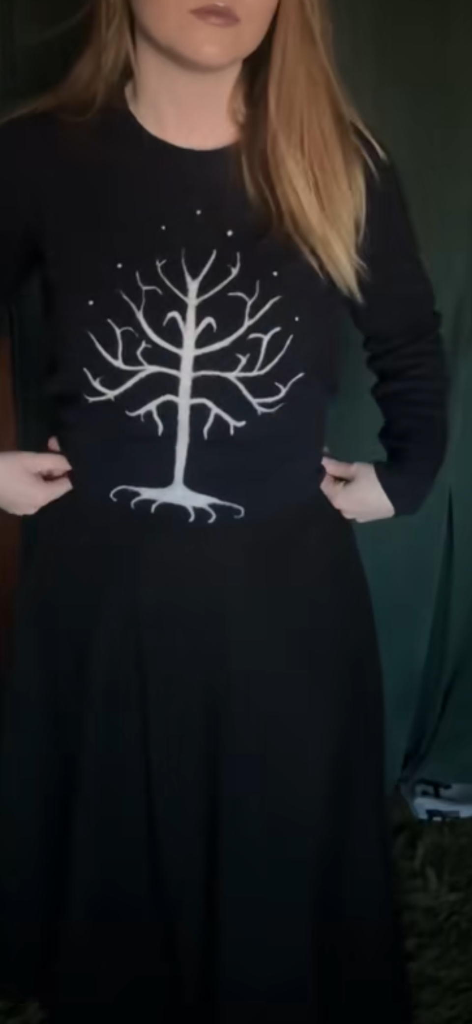 A woman wearing a black sweater with a white, stylized tree design on the front.