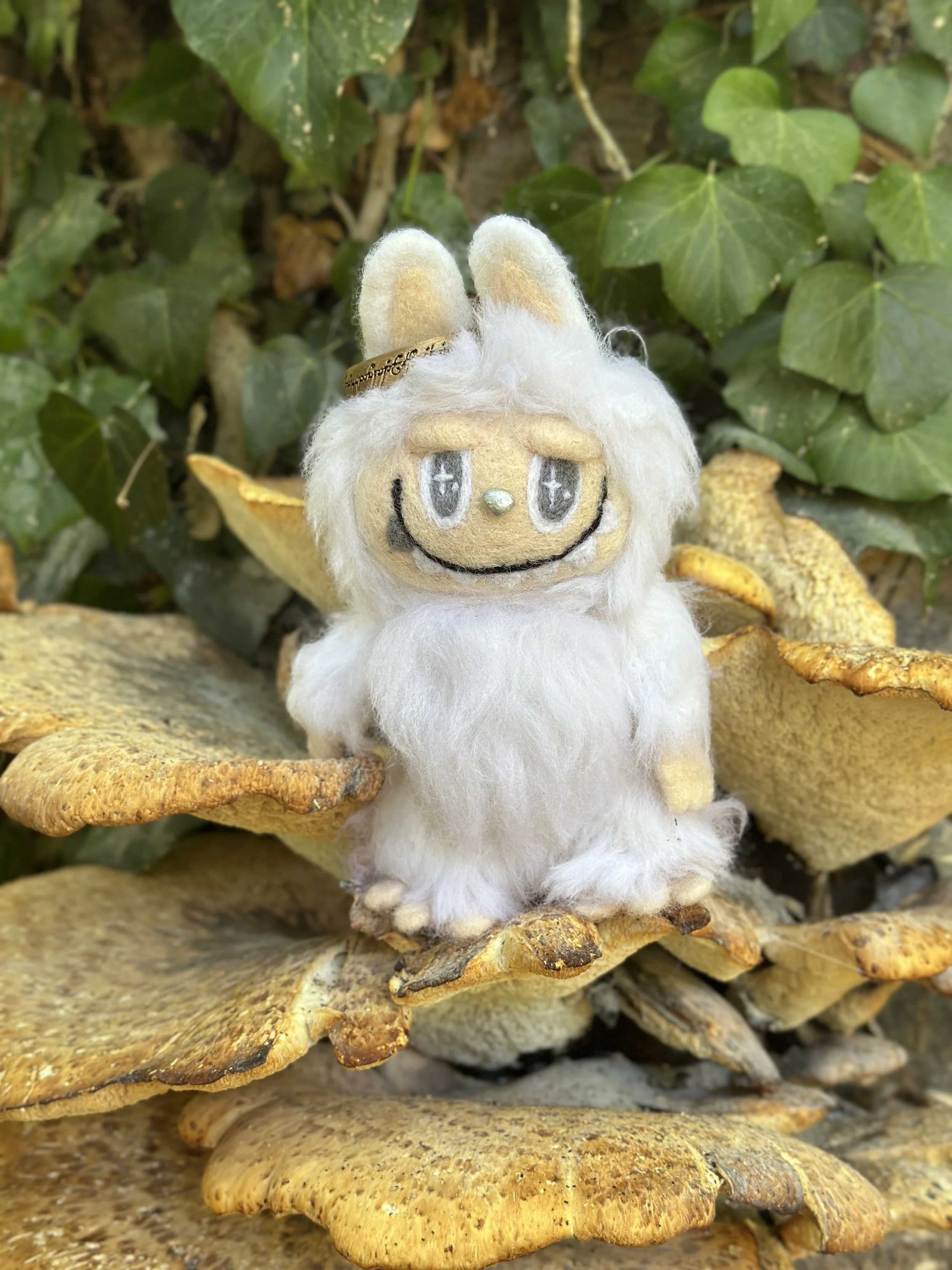 A felted lafufu, sitting among yellowish fungi and green ivy leaves.