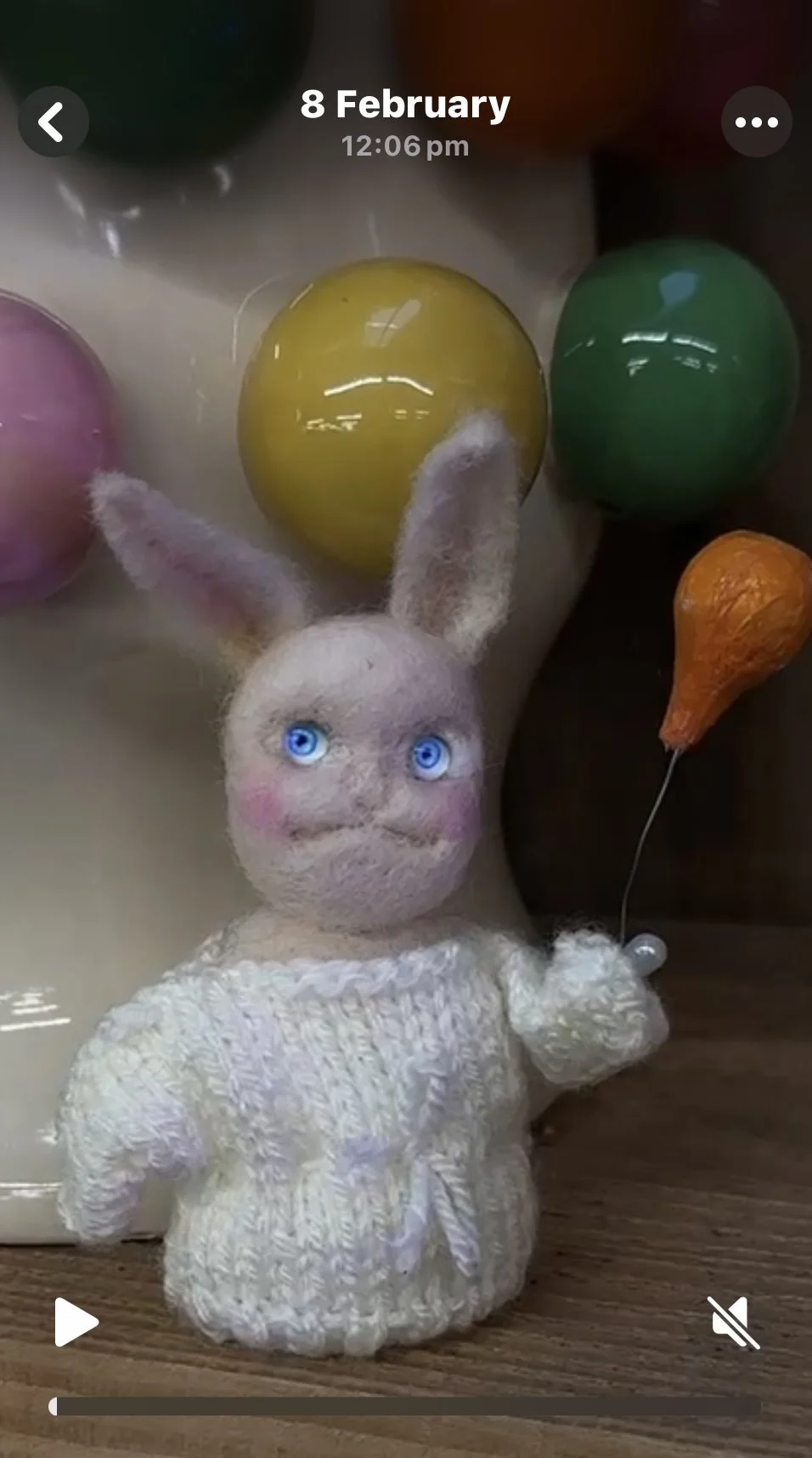 Felt bunny holding an orange balloon, surrounded by colored eggs on a table.