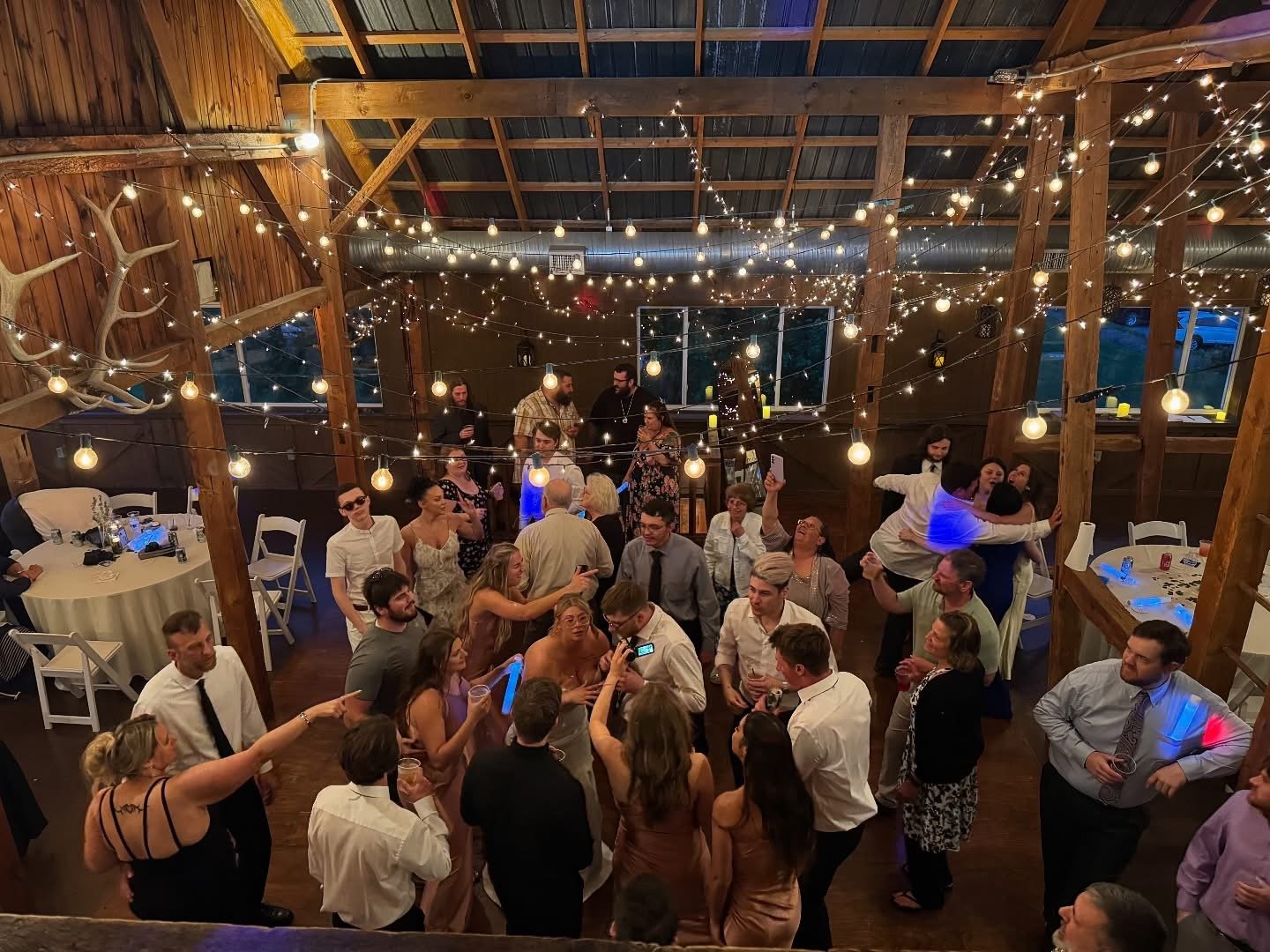 People dancing and socializing in a rustic barn with string lights and decorations for a celebration or party.