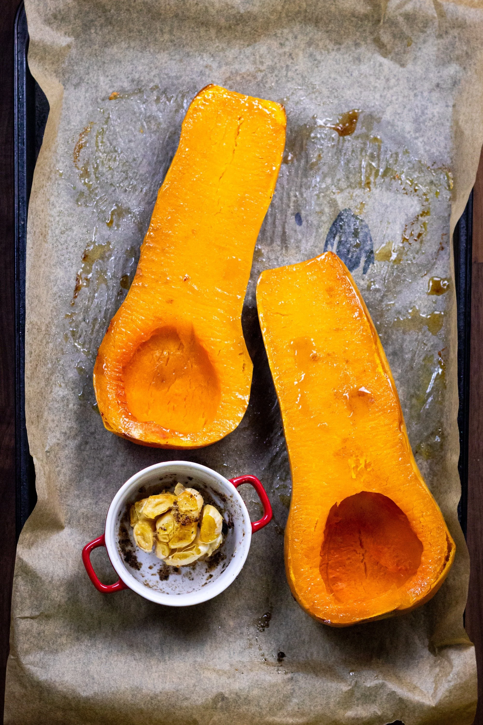Butternut squash halves and a foil-wrapped head of garlic on a baking sheet.
