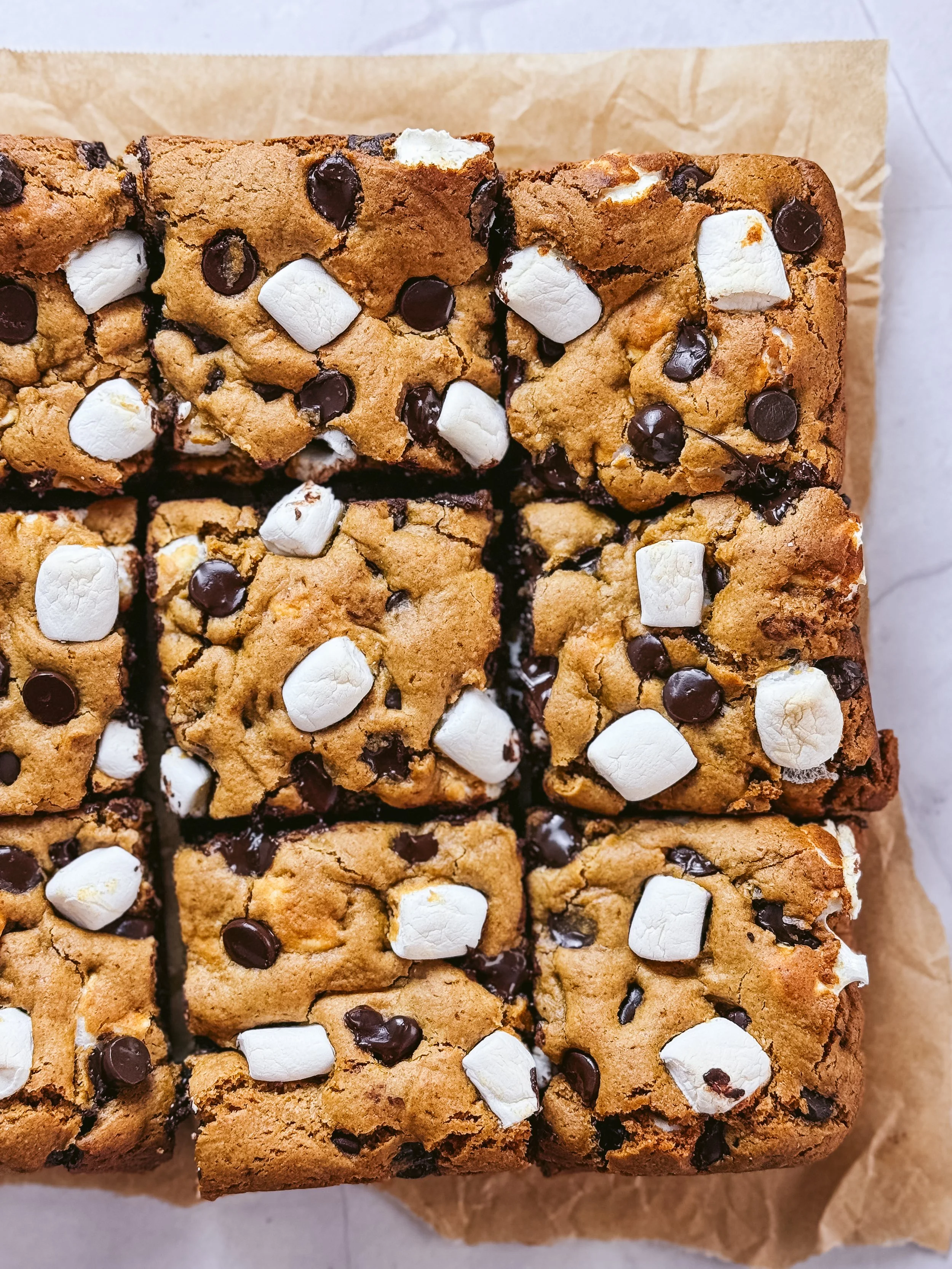 Close-up of sliced blondies with golden tops, chocolate chips and white marshmallows on parchment.