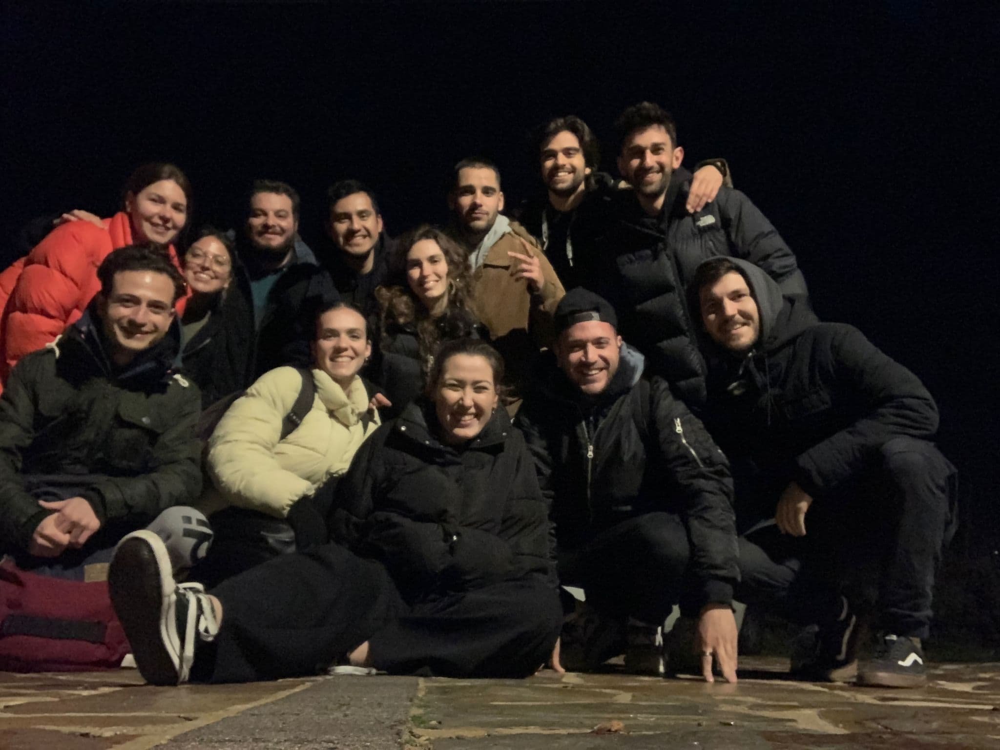 Grupo de personas sonrientes en la noche, con ropa de abrigo, posando juntos en una superficie de piedra.