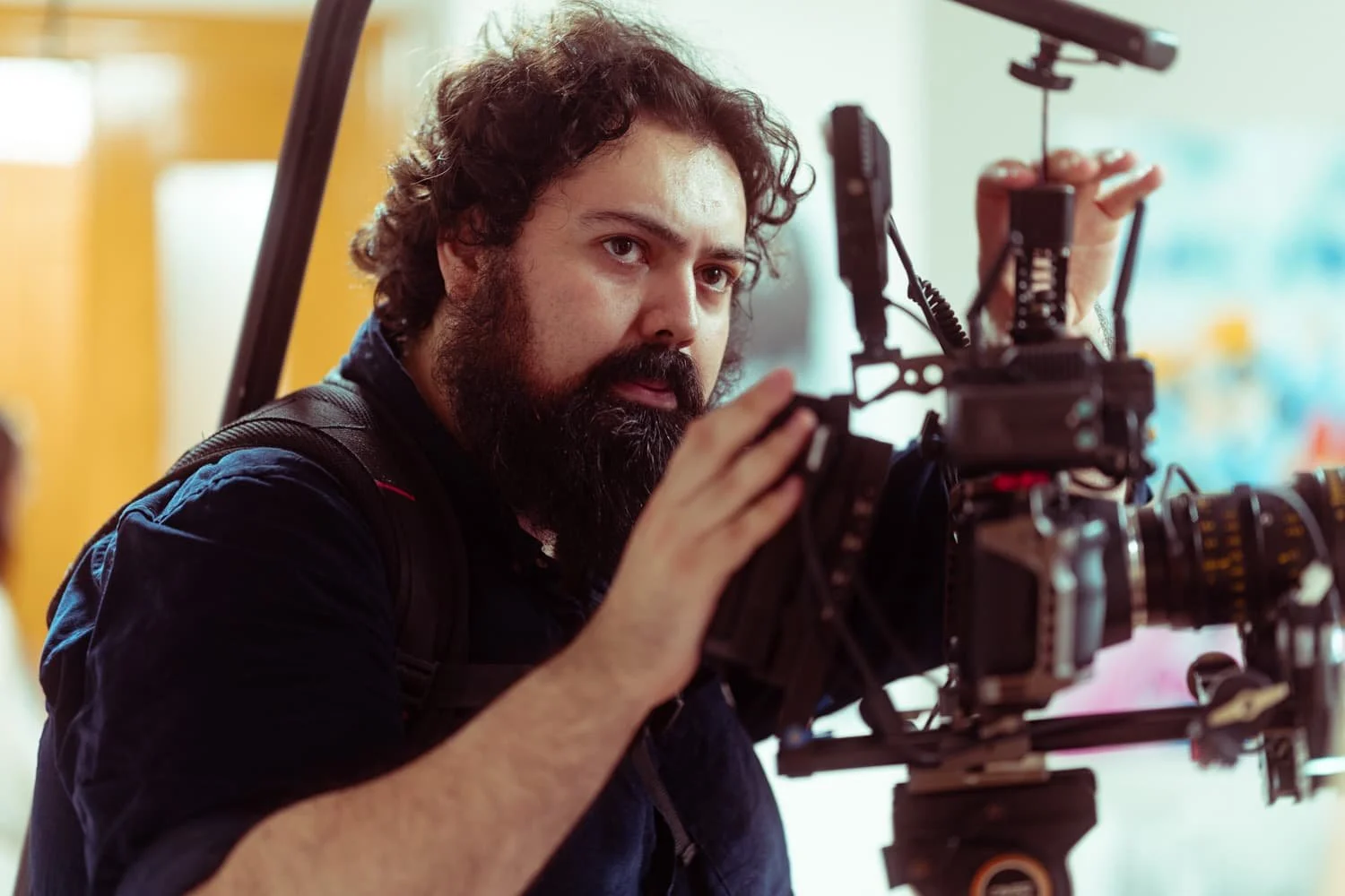 Hombre con barba y cabello rizado ajustando equipo de cámara en interior