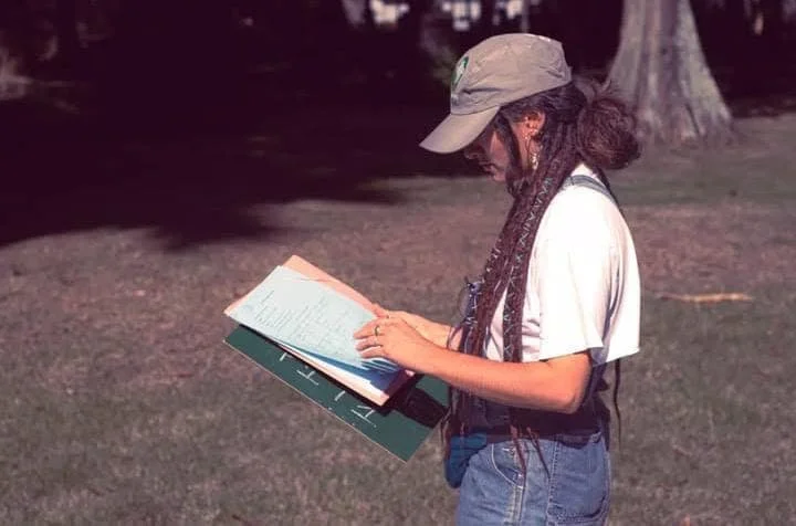 Una persona con gorra y cabello trenzado leyendo un libro en un parque