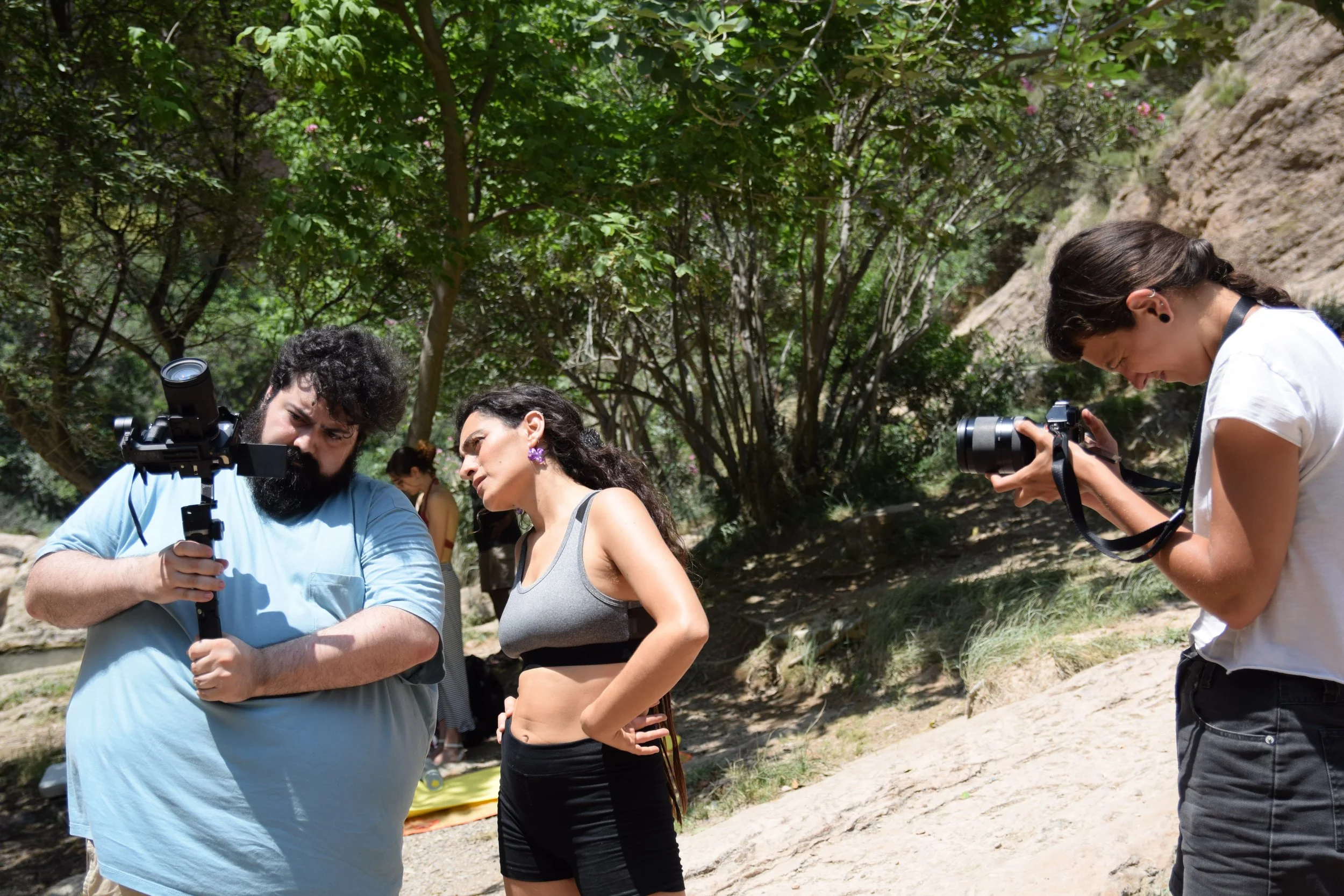 Tres personas en un entorno natural, dos sosteniendo cámaras y una otra con un dispositivo de grabación, aparentemente participando en una grabación o sesión fotográfica al aire libre