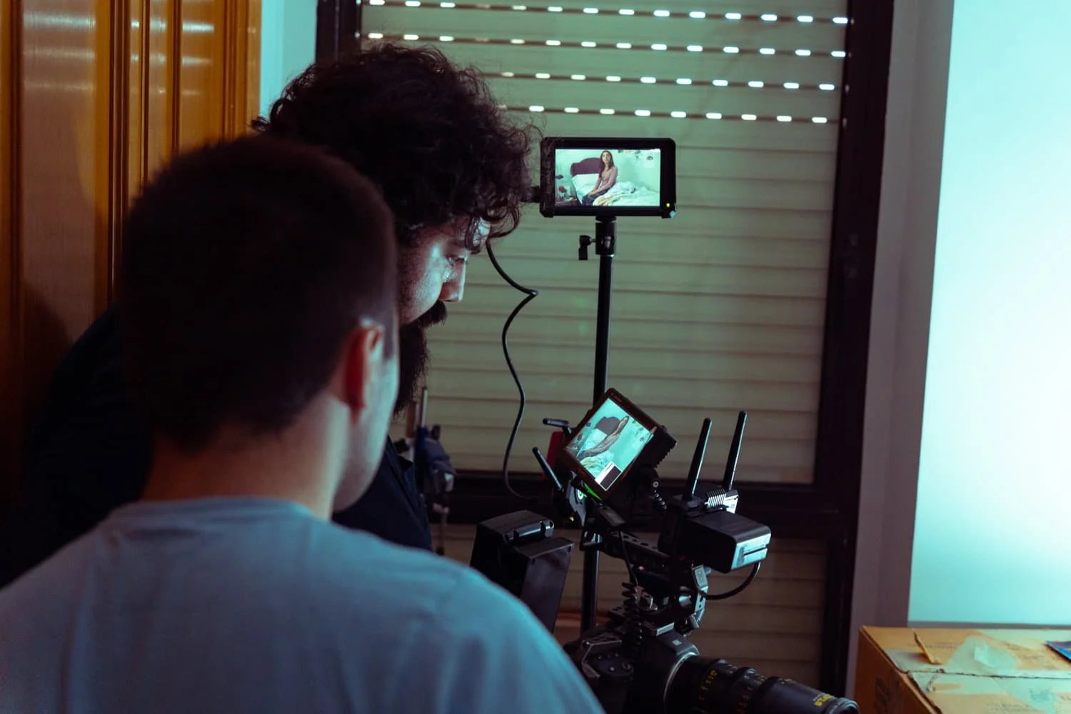 Un equipo de filmación captura una escena en un entorno interior, con una cámara montada en un trípode y dos personas observando atentamente la grabación en pantalla.