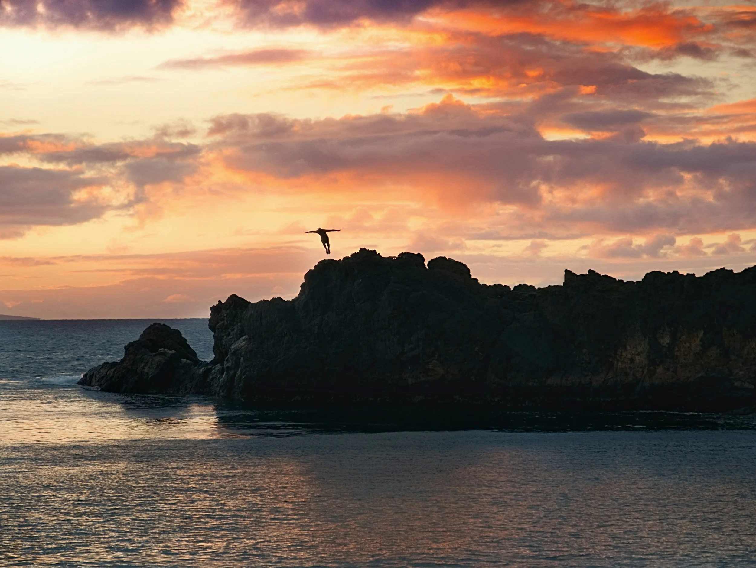 cliff diver jumping from Black Rock in Kaanapali, Maui at sunset with ocean views