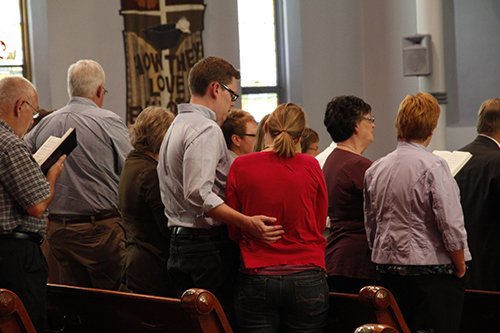 couple standing and singing in a church service among other parish members