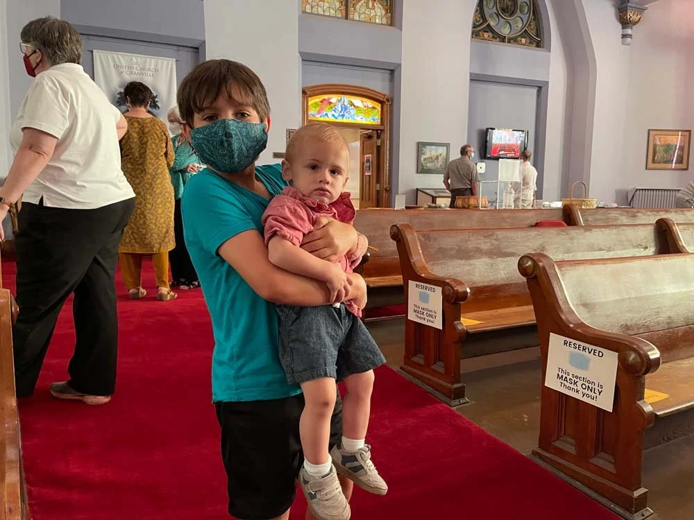 a young person holding a baby wearing a mask looking at the camera