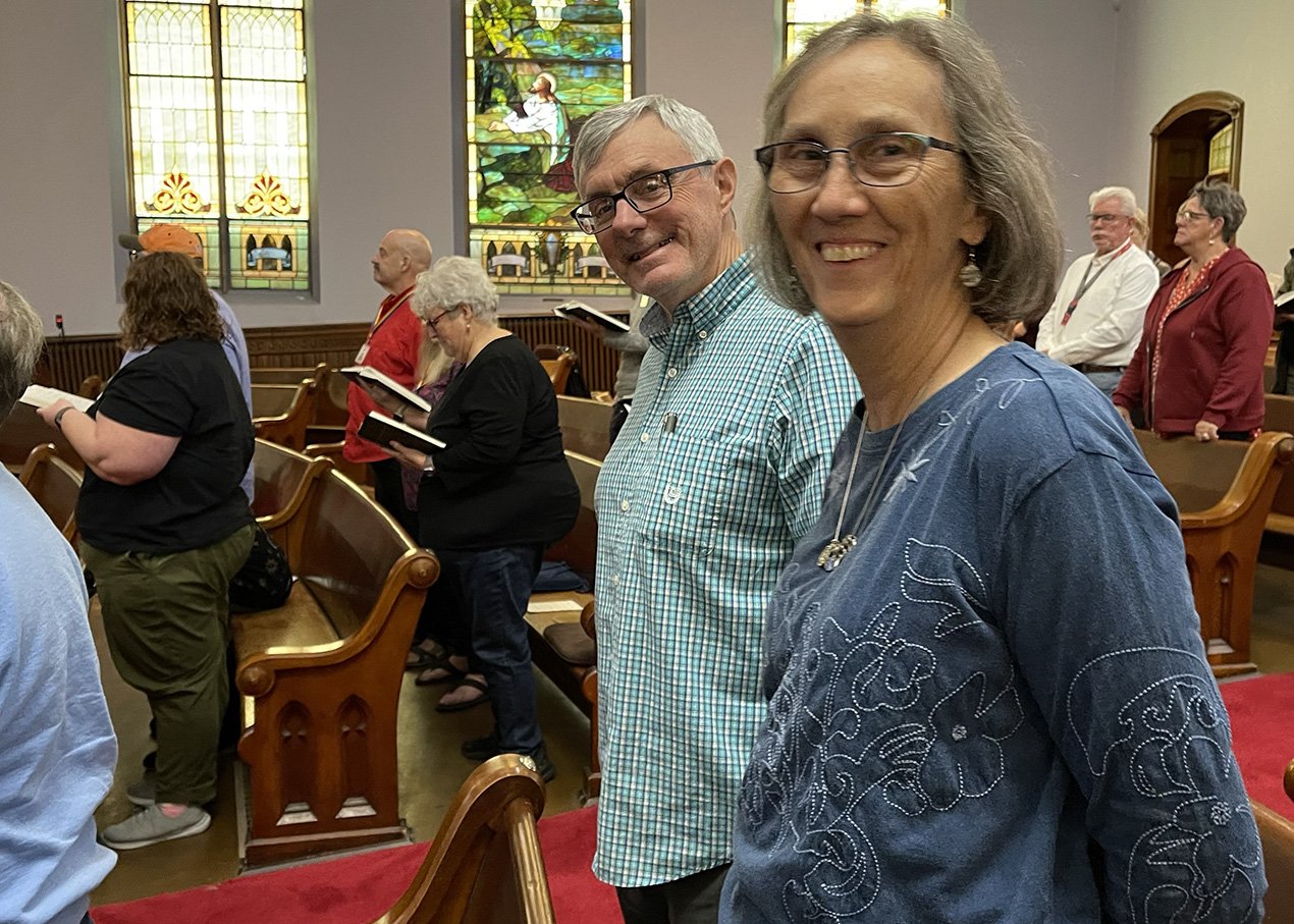 smiling congregants in service while others are singing and view of windows in sanctuary behind