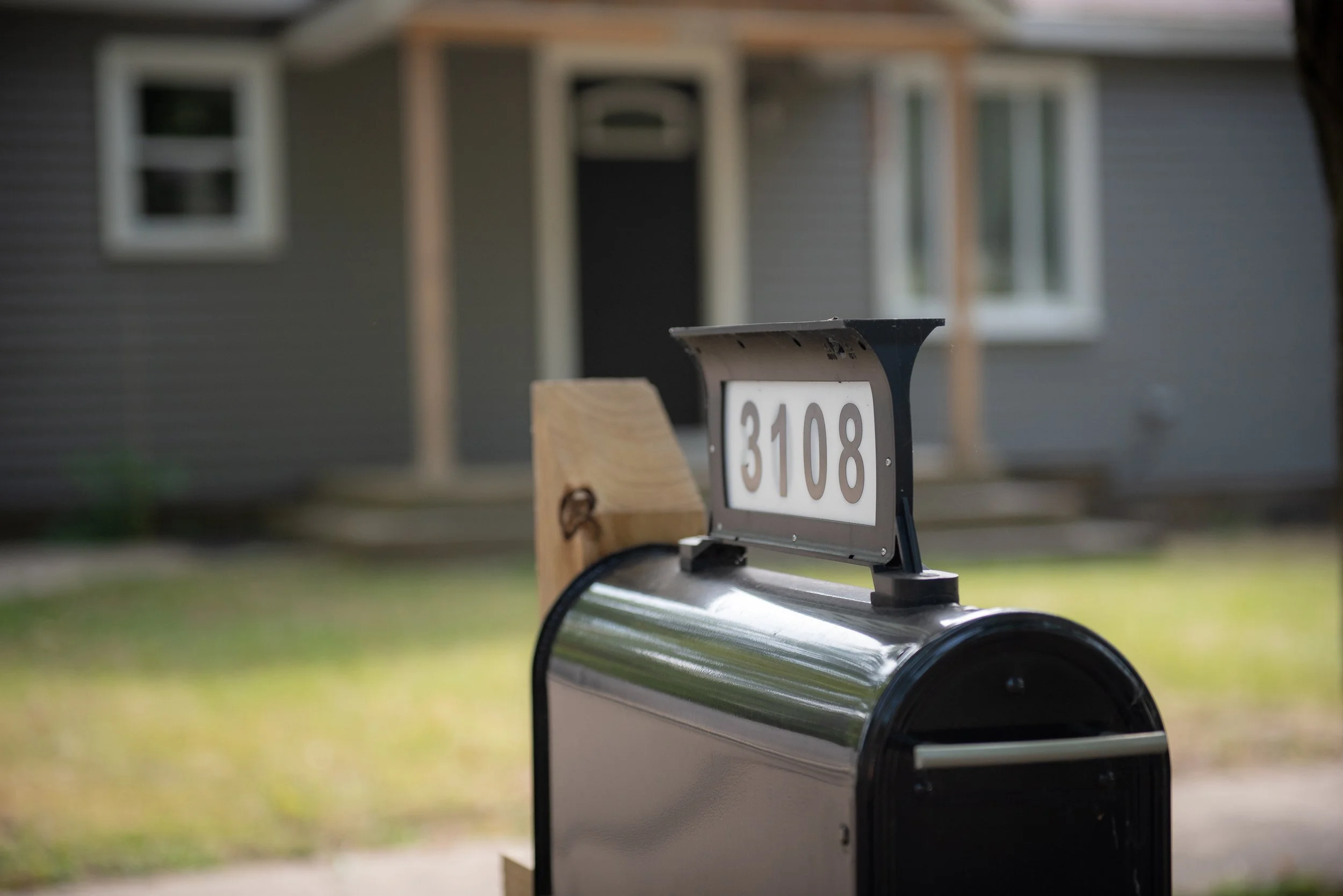Mailbox with house number 3108 in front of a house with grey siding and white window frames.