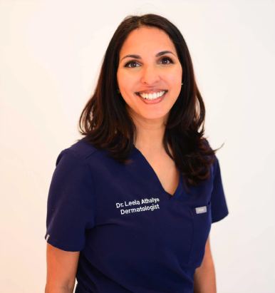 Portrait of a smiling woman with shoulder-length dark hair, wearing a navy blue medical scrubs top with text that reads 'Dr. Leela Athavale Dermatologist', in front of a plain white background.
