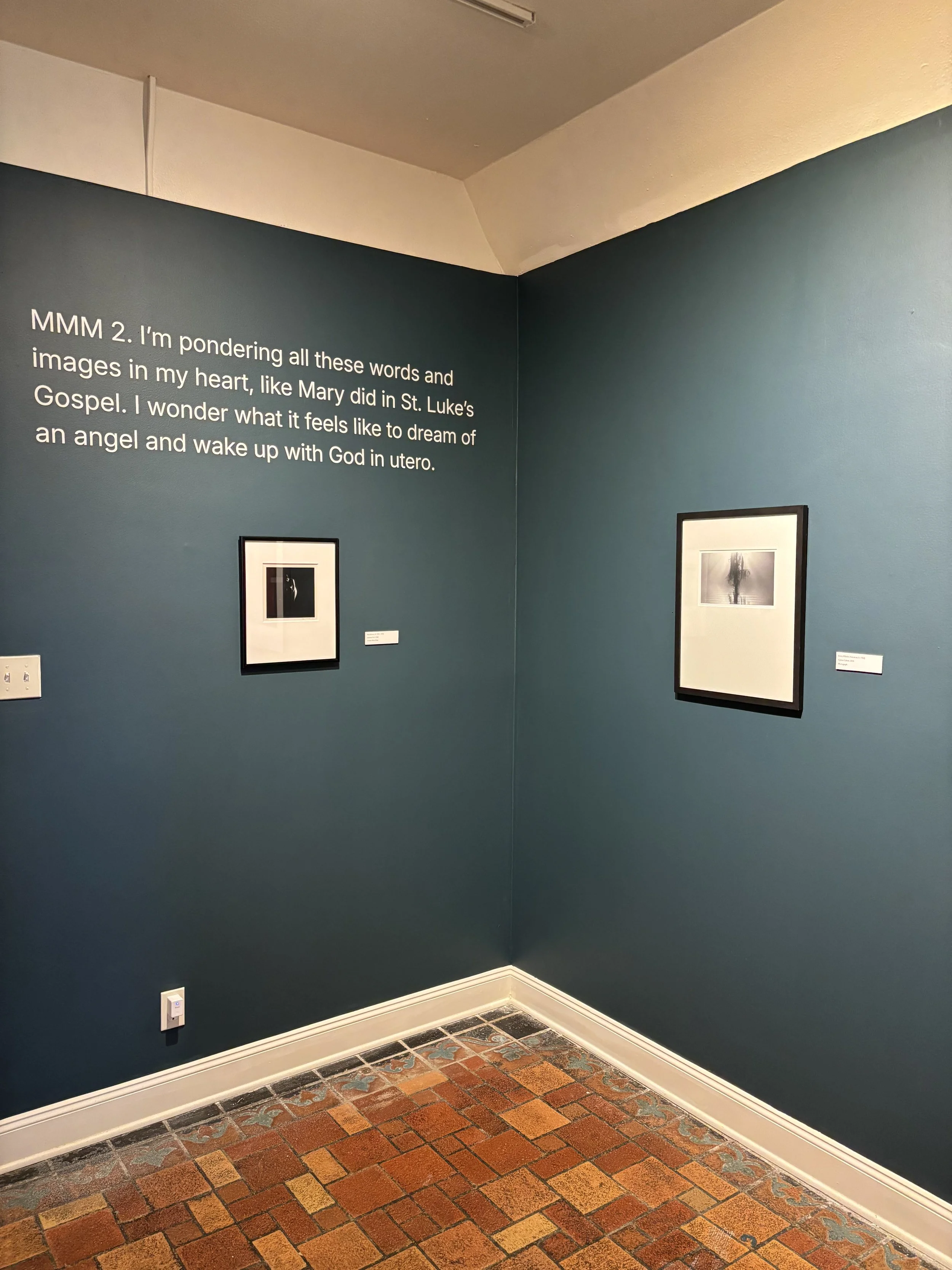 Museum wall with a quote about pondering words and images, accompanied by two framed photographs and a tiled floor.