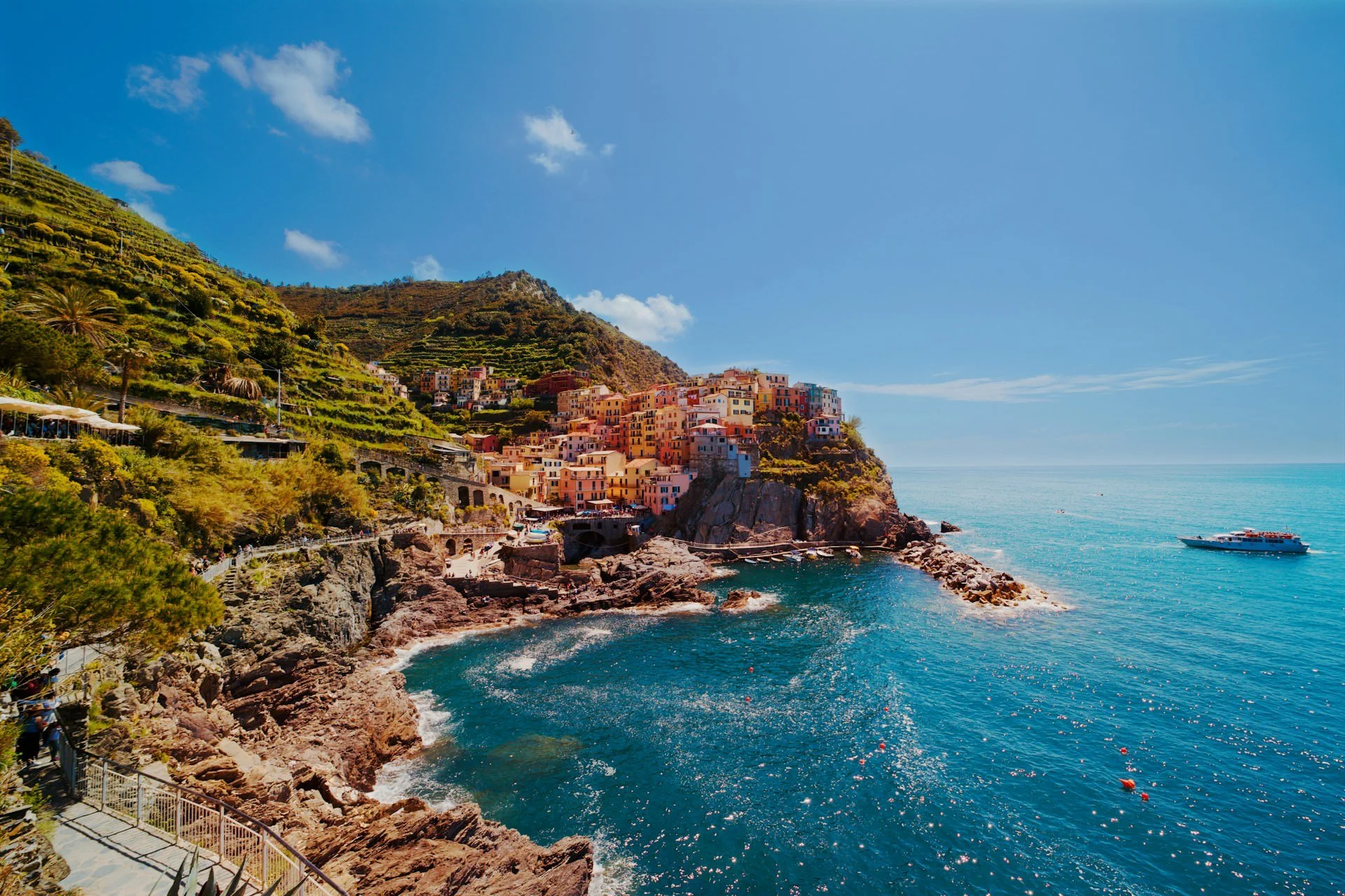 panoramic view of Cinque Terre coastline with rocky cliffs, hillside village, and bright blue Mediterranean water