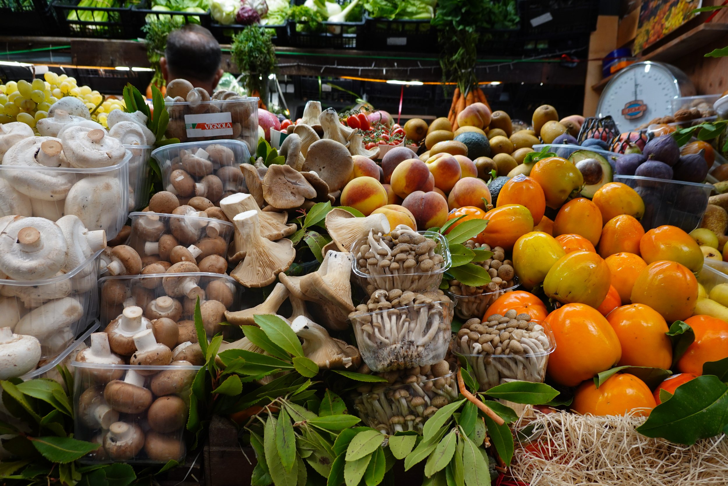 Fresh mushrooms, peaches, citrus fruits, and seasonal produce displayed at a colorful Italian market in Sardinia.