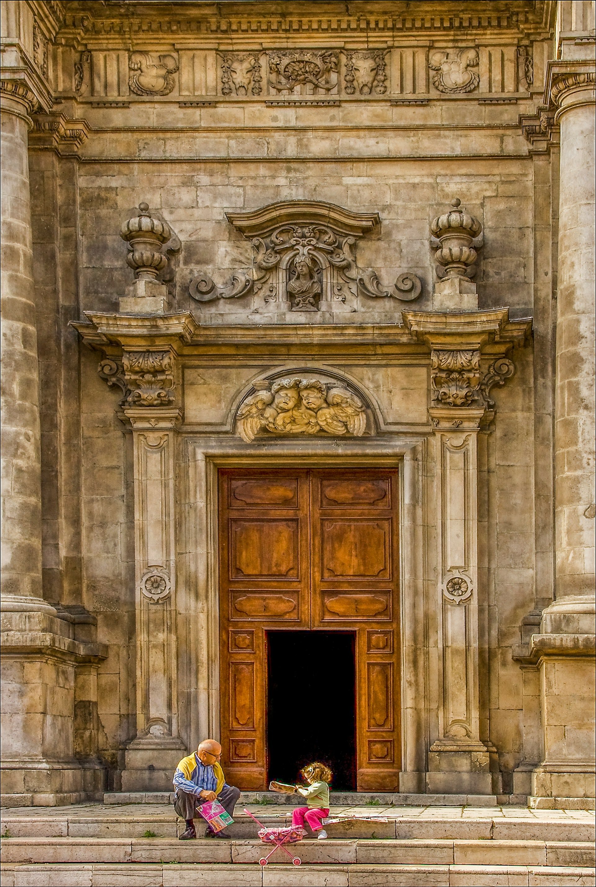 Grandfather sitting on church steps in Italy reading with his granddaughter in front of historic stone cathedral doorway