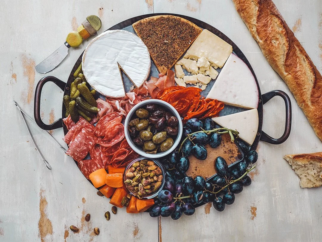 Cheese and charcuterie board with grapes, pickles, nuts, and bread.