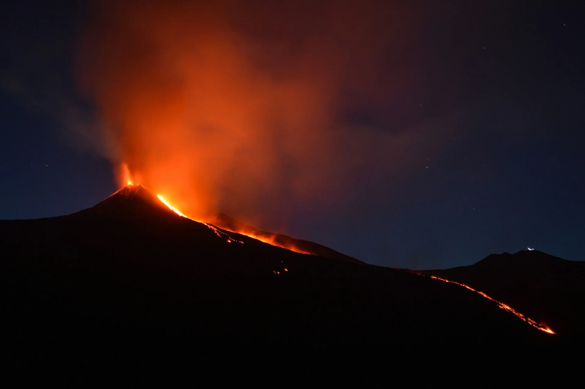 Mount Etna erupting at night with glowing lava flowing down the volcano in Sicily