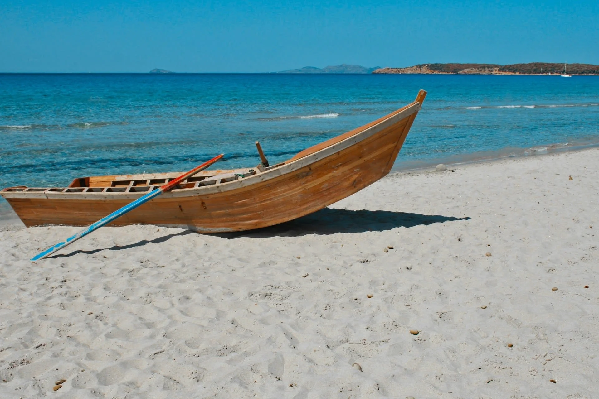 Traditional wooden boat resting on a white sand beach beside clear turquoise Mediterranean water in Sardinia, Italy.