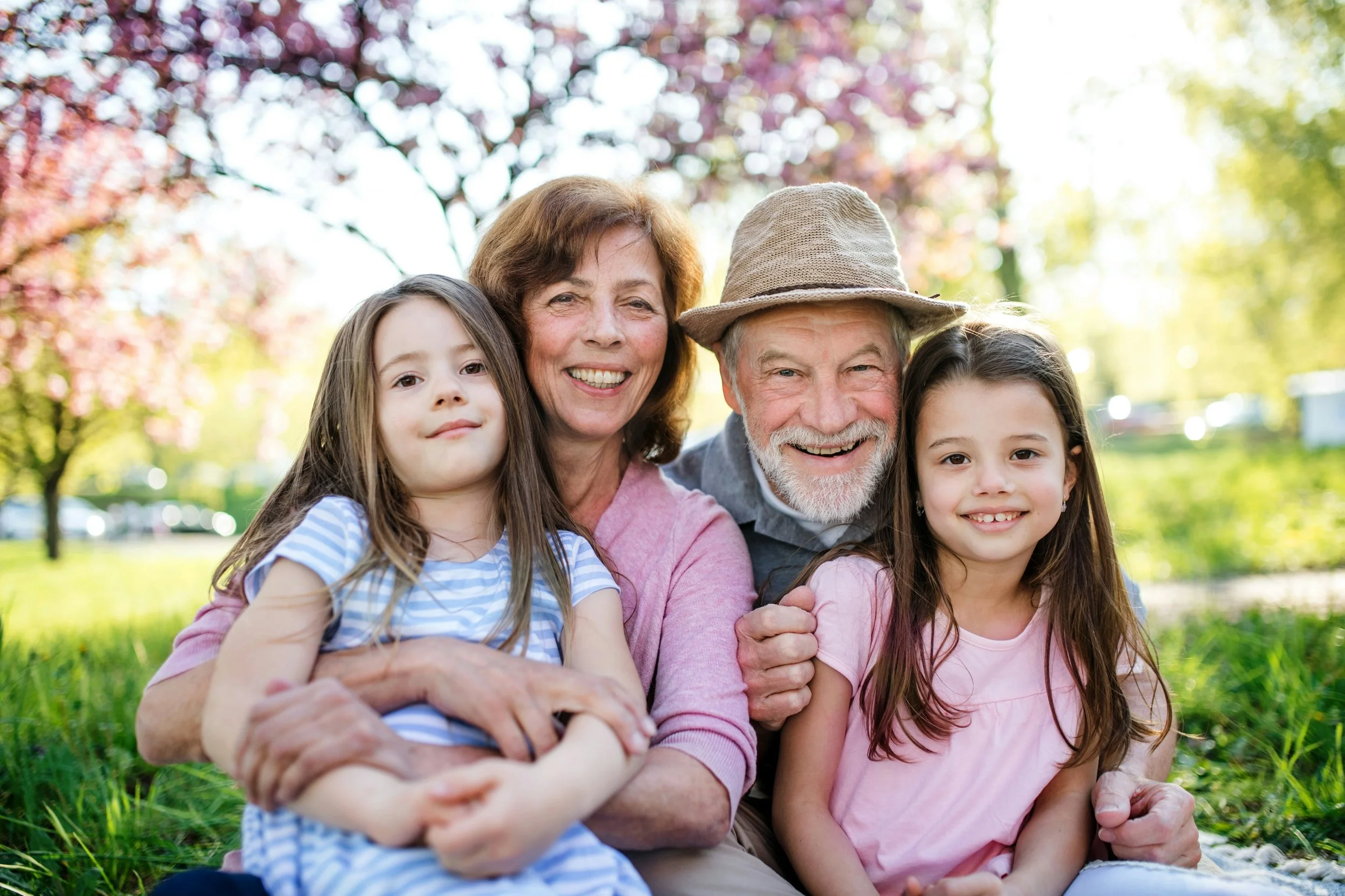 Grandparents smiling with two young granddaughters outdoors, representing joyful multigenerational family travel