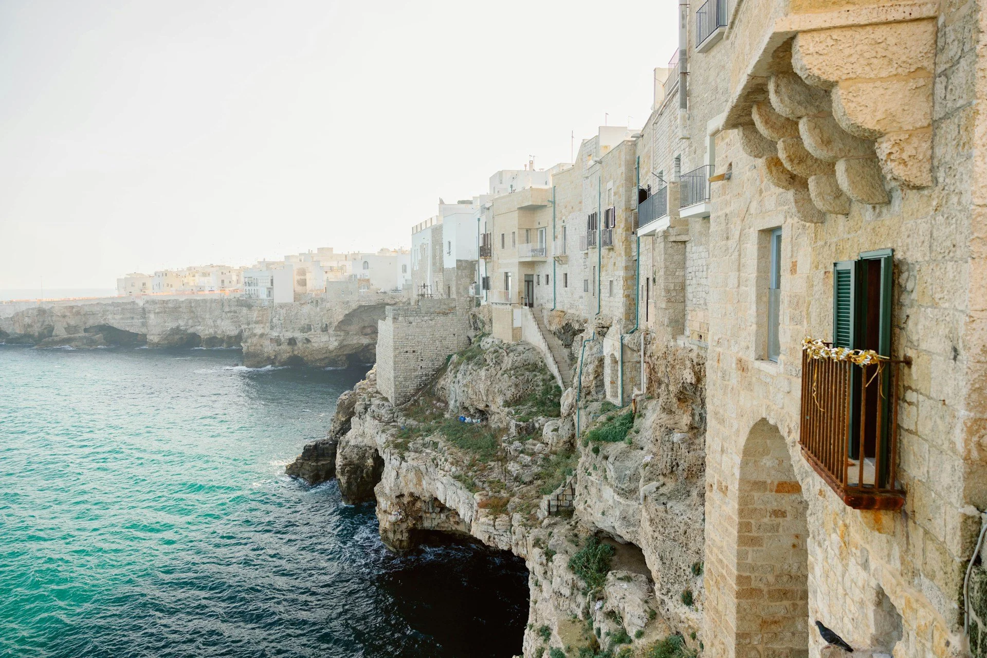 Historic stone buildings perched along the rocky coastline above turquoise water in Polignano a Mare, Puglia, Italy.