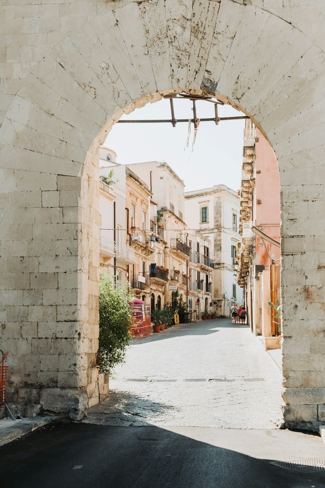 Historic stone archway framing a sunlit street with traditional buildings in Sicily, Italy.