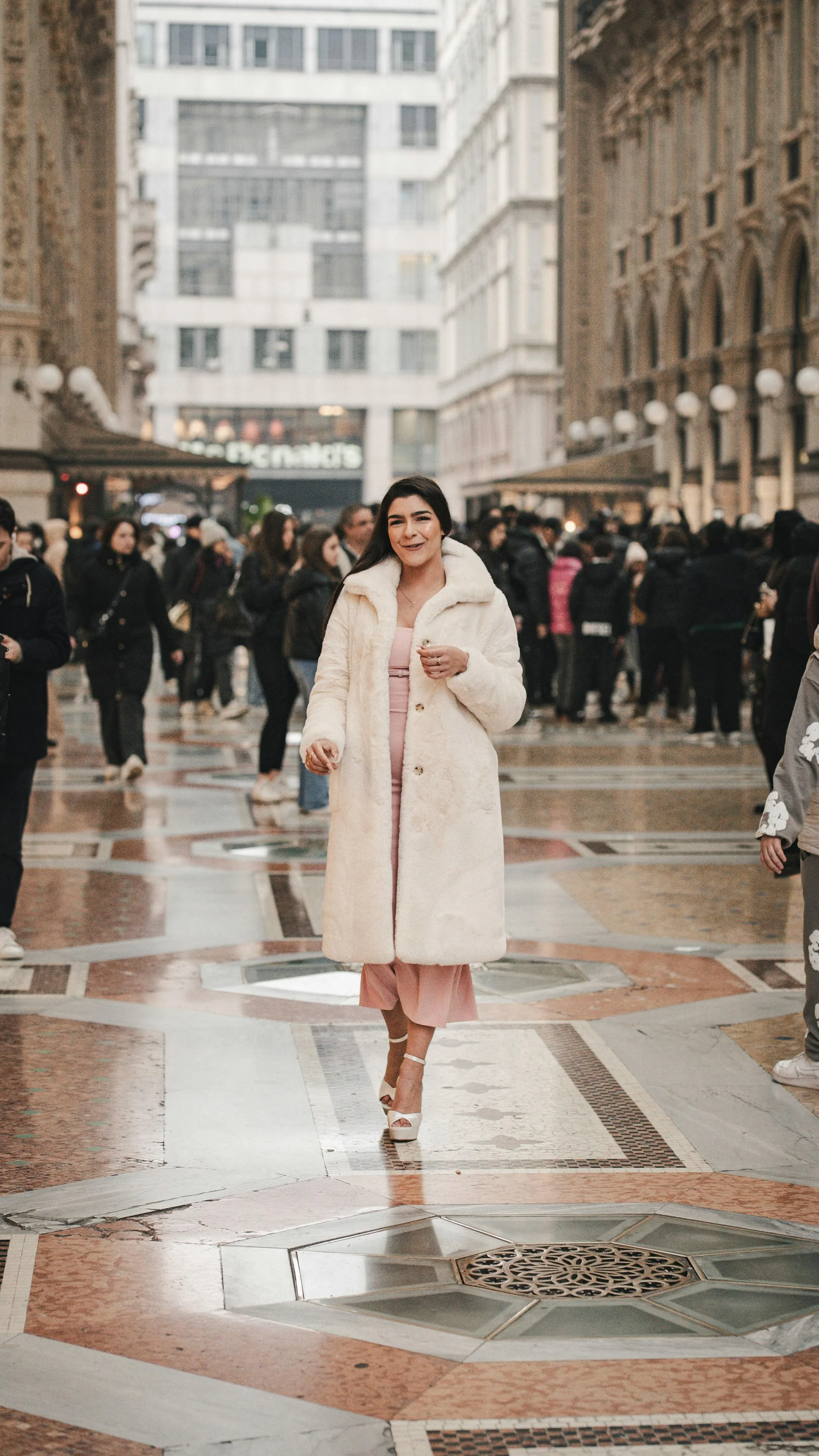 woman standing in the street in milan with pink gown and white fur coat in heels