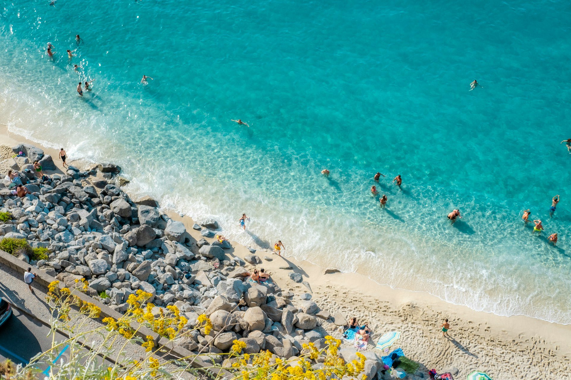 Swimmers enjoying turquoise waters along a sandy and rocky beach on the coast of Calabria, Italy