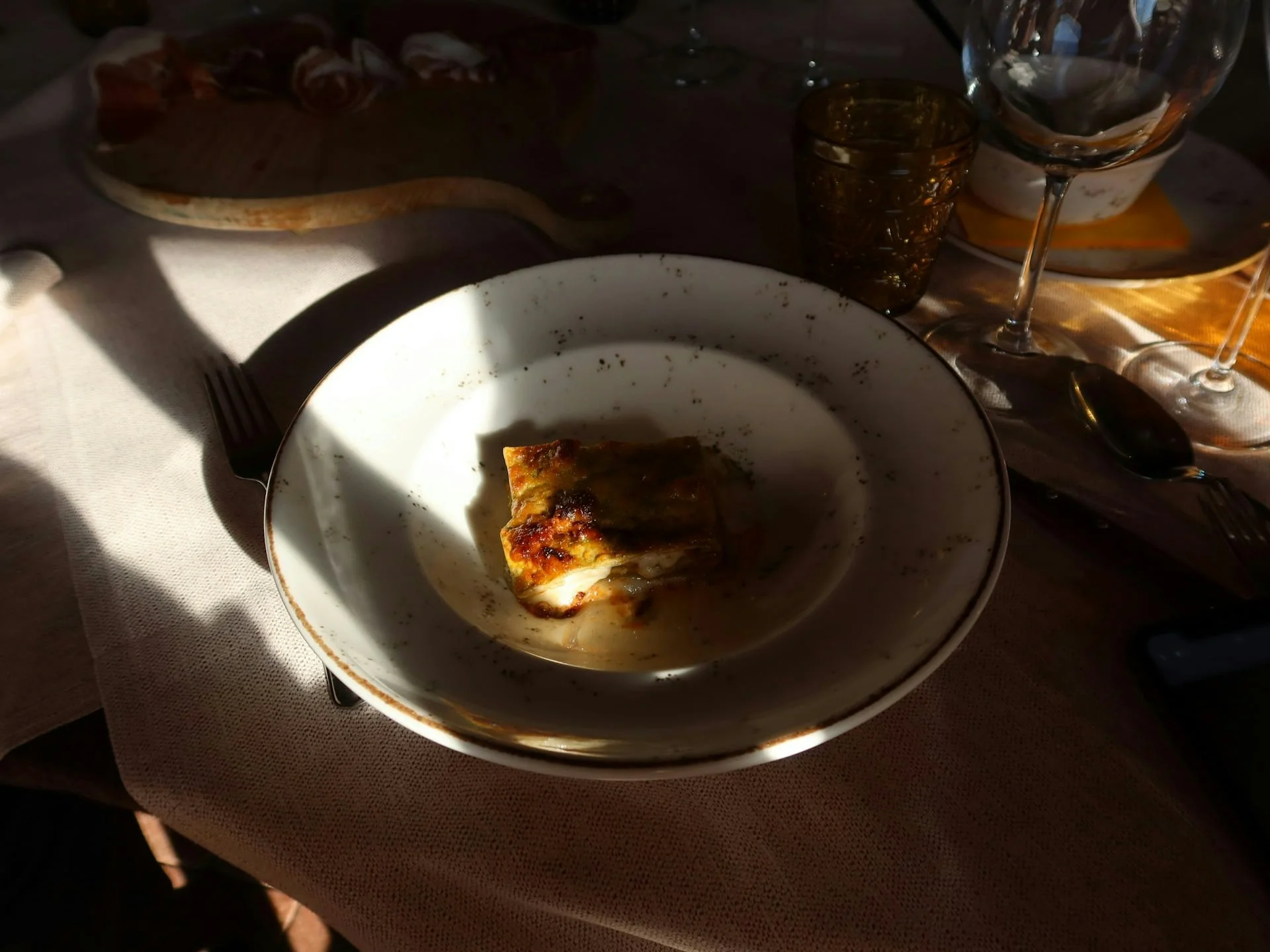 Elegant Italian dish served on a white plate in warm golden light at a restaurant table, with wine glasses and a charcuterie board in the background, capturing a relaxed evening dining experience in Italy