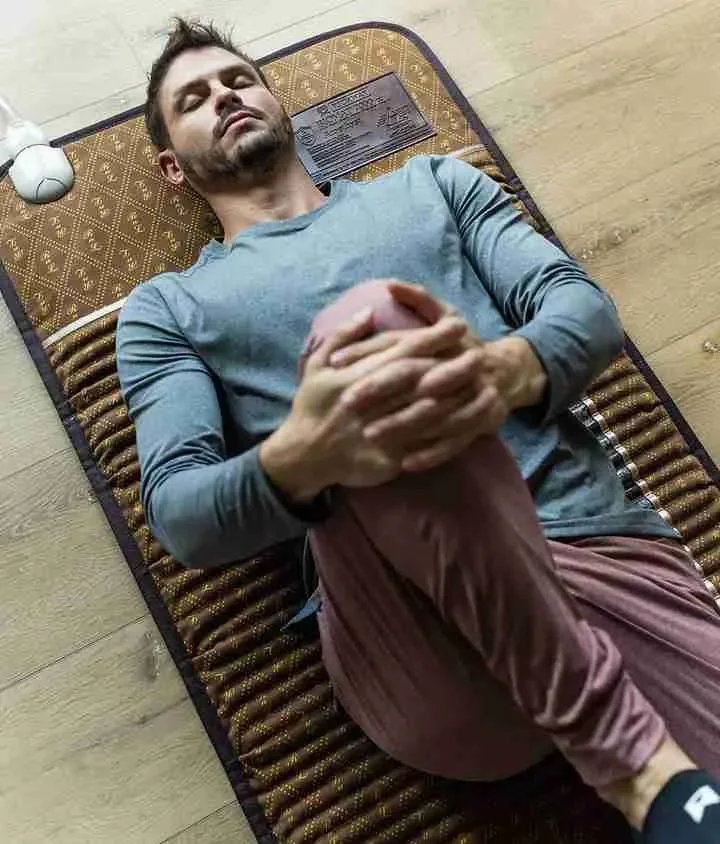 A man lying on a prayer mat with his hands clasped over his abdomen, eyes closed, and a peaceful expression.